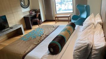 Habitación de hotel con una cama grande, un escritorio, una silla y una ventana con vista a la ciudad.