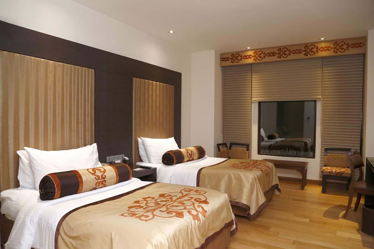 Ein Hotelzimmer mit zwei Betten, einem großen Spiegel, einem Fernseher und einem Holzboden.
