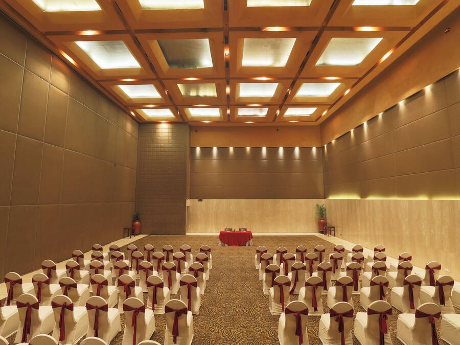 Un salón de conferencias con filas de sillas blancas, una mesa roja al frente y un techo alto con tragaluces.