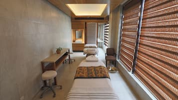 Habitación de spa con camilla de masaje, un escritorio pequeño, una silla y un ventanal con persianas.