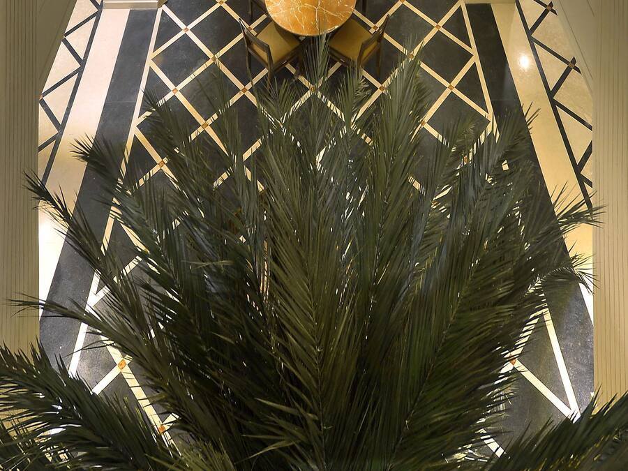 A multi-level atrium with a central walkway, palm trees, and a decorative floor pattern.