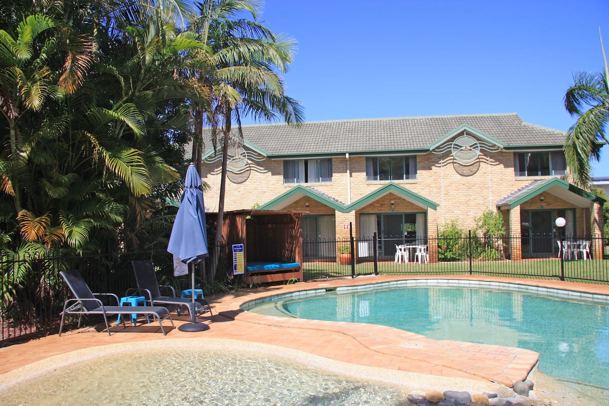 A hotel with a swimming pool, lounge chairs, and palm trees.