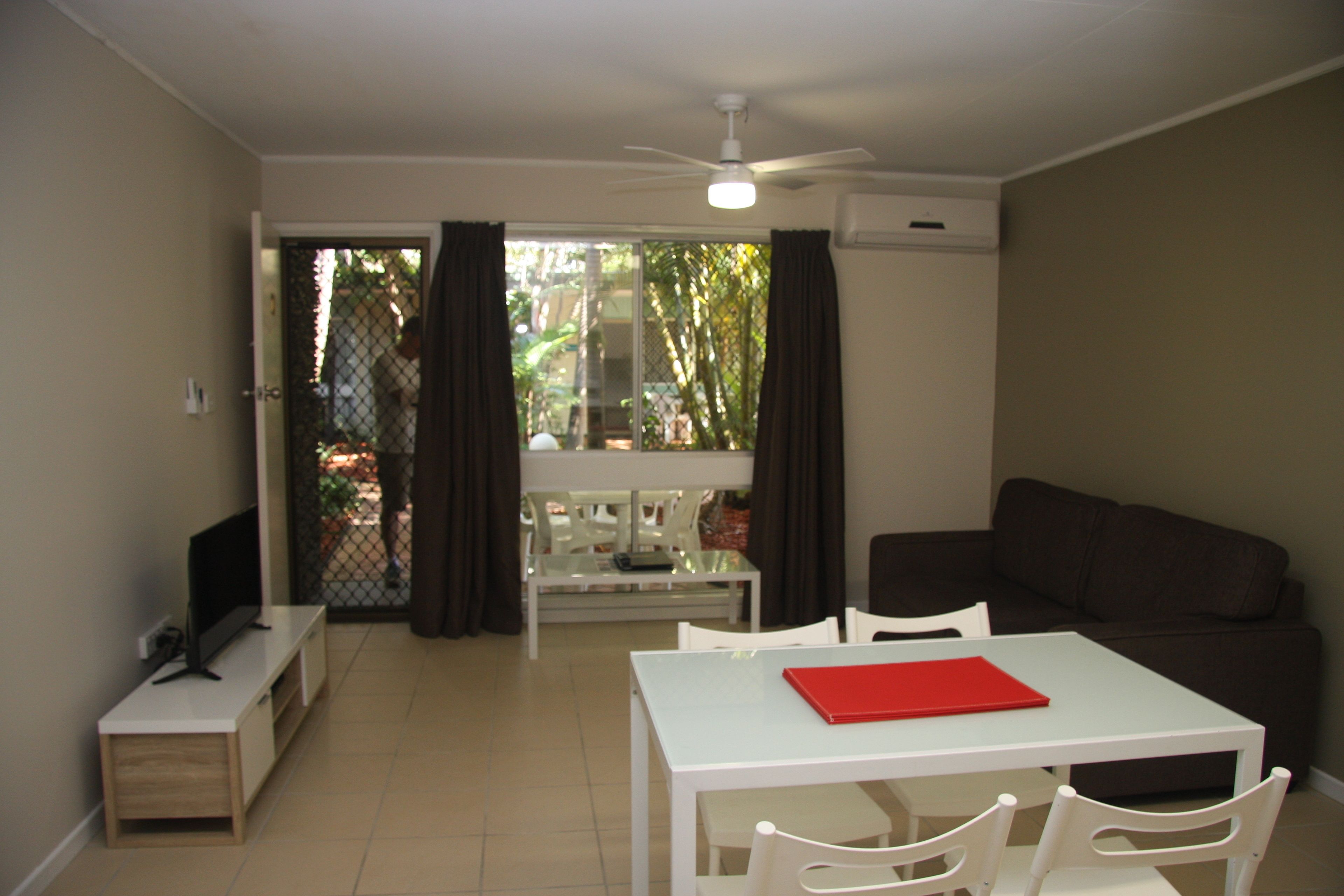 A living room with a white table, a brown sofa, and a TV on a wooden stand.