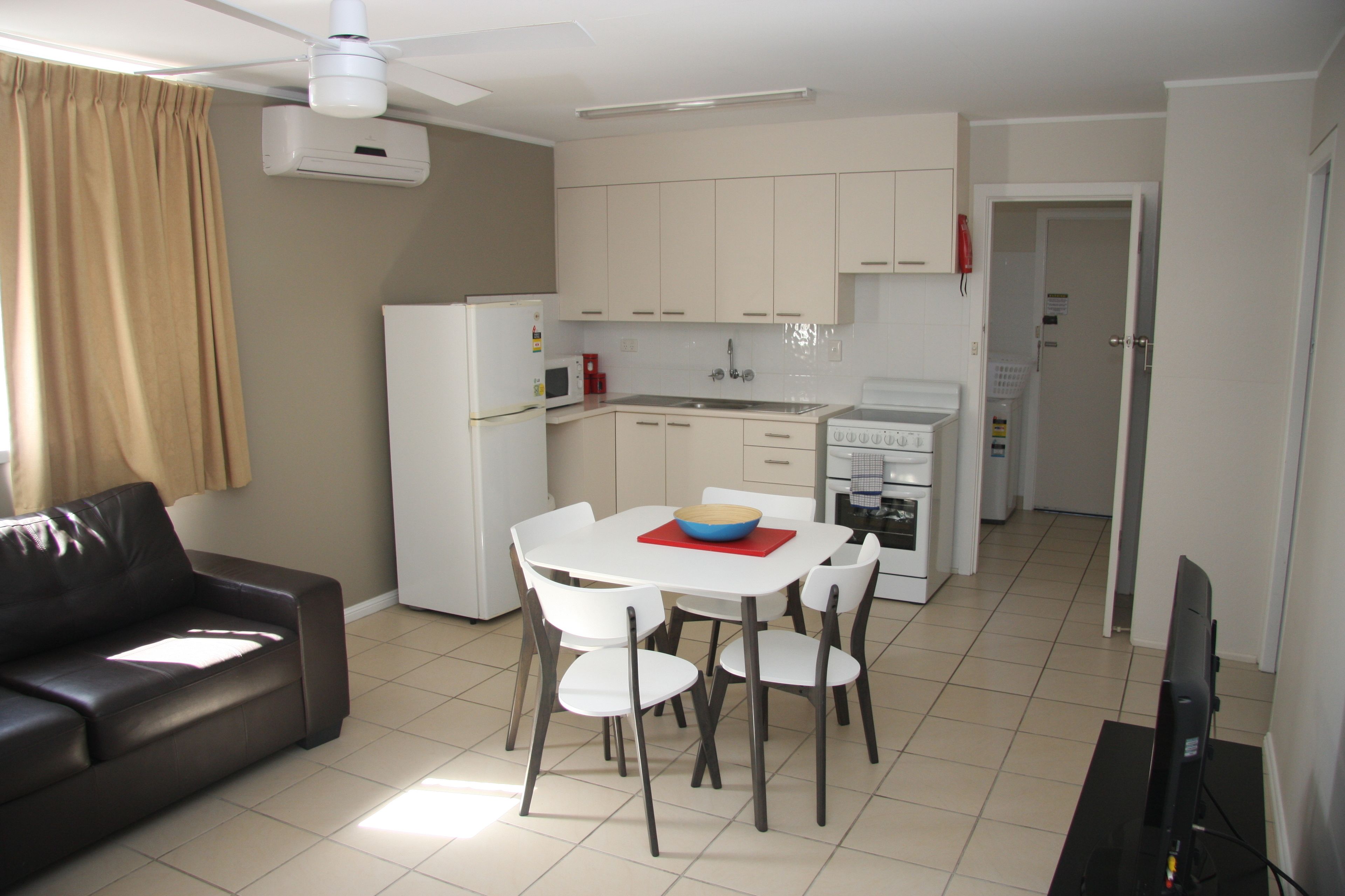 Una cocina moderna con armarios blancos, una mesa de comedor con sillas, un refrigerador y un microondas.