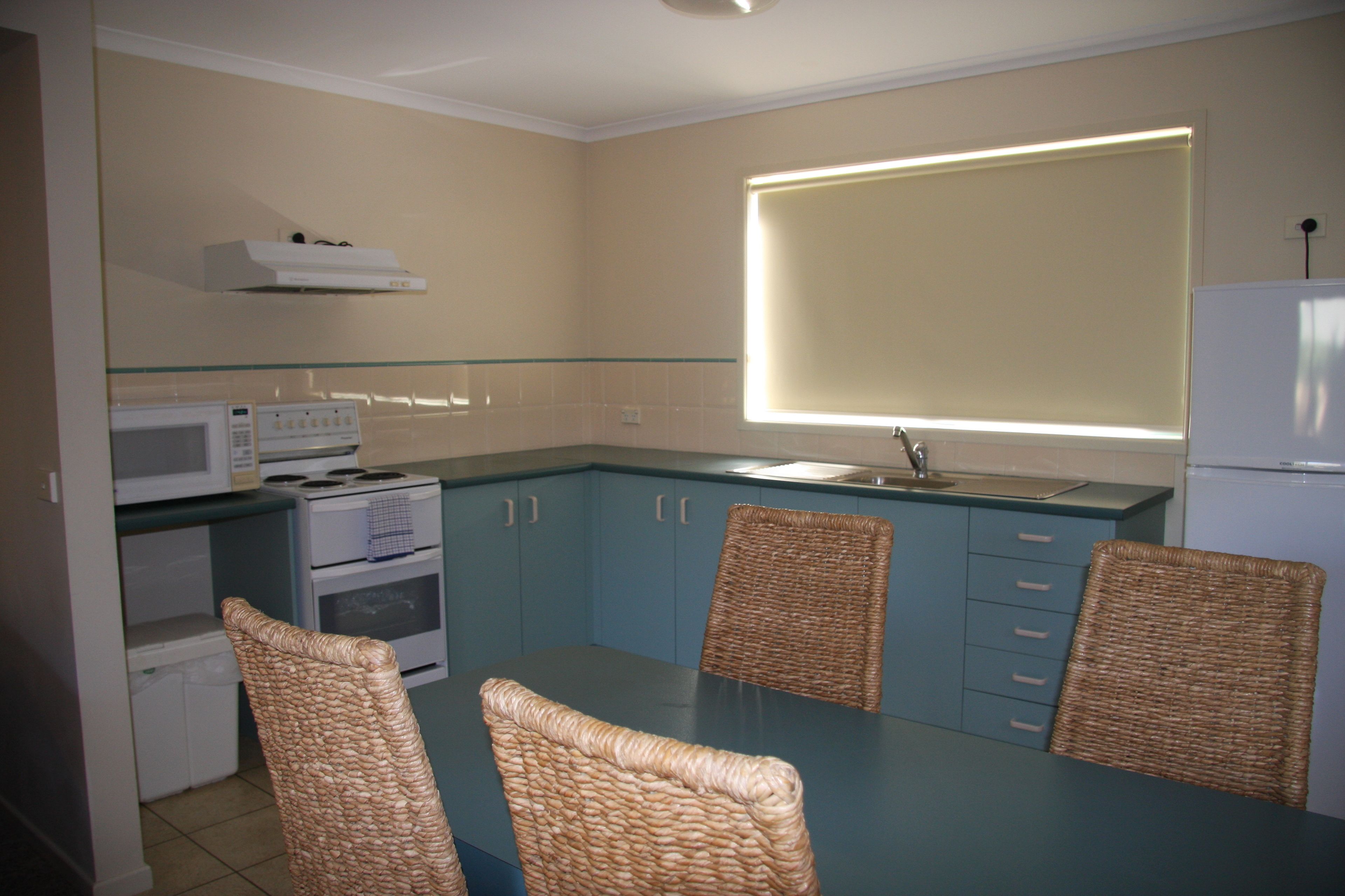 Une cuisine compacte comprenant une table à manger, quatre chaises en osier, un four à micro-ondes, une cuisinière et un réfrigérateur.