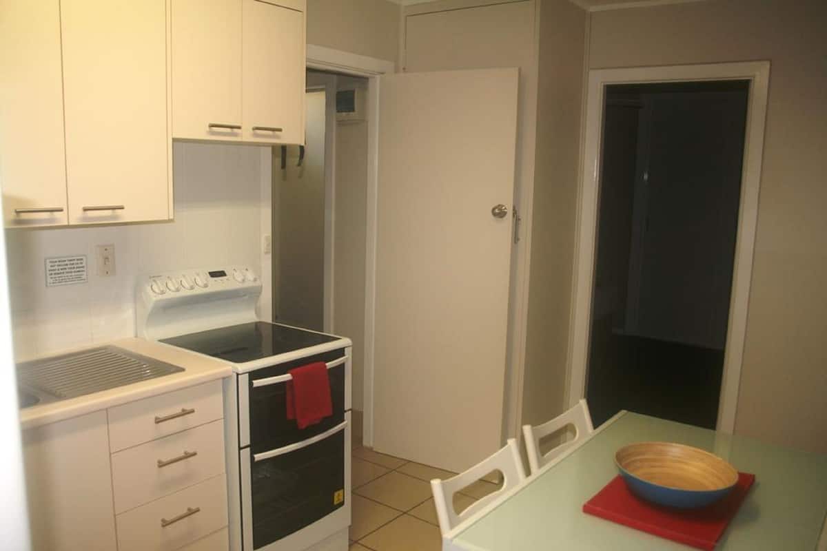 A compact kitchen with white cabinets, a stove, and a small dining table with a bowl.