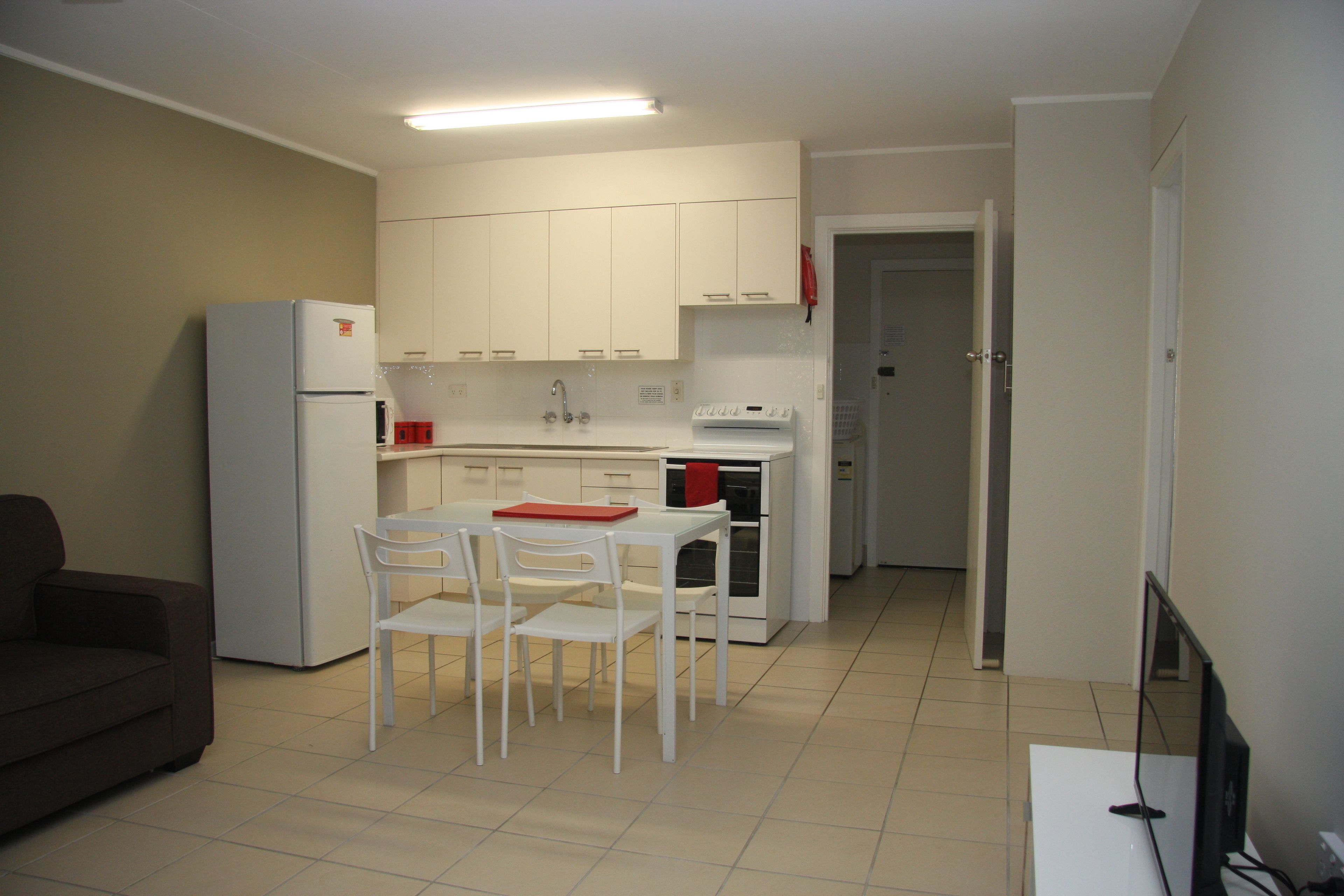 A compact kitchen with white cabinets, a refrigerator, a stove, and a dining area with a table and chairs.