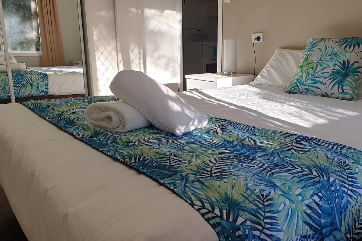 A hotel room with a bed, a bedside table, a lamp, and a view of the outside.