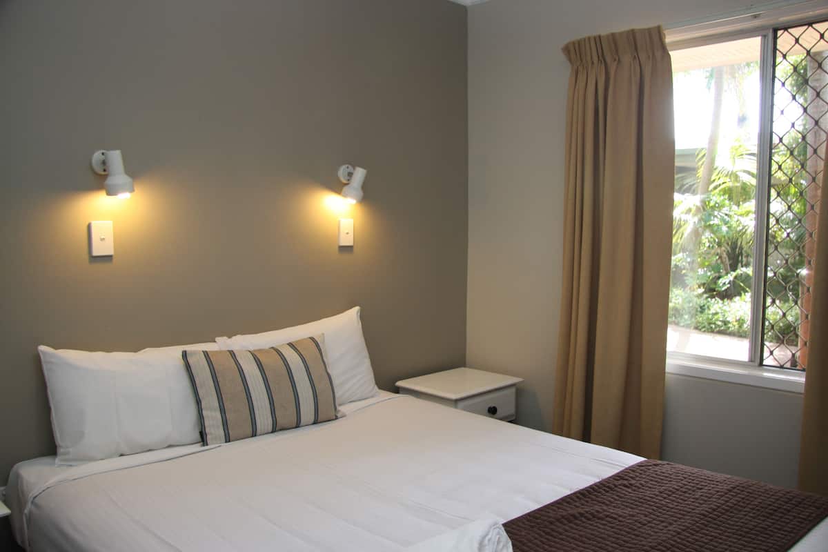 A bedroom with a bed, two wall-mounted lights, a nightstand, and a window with curtains.