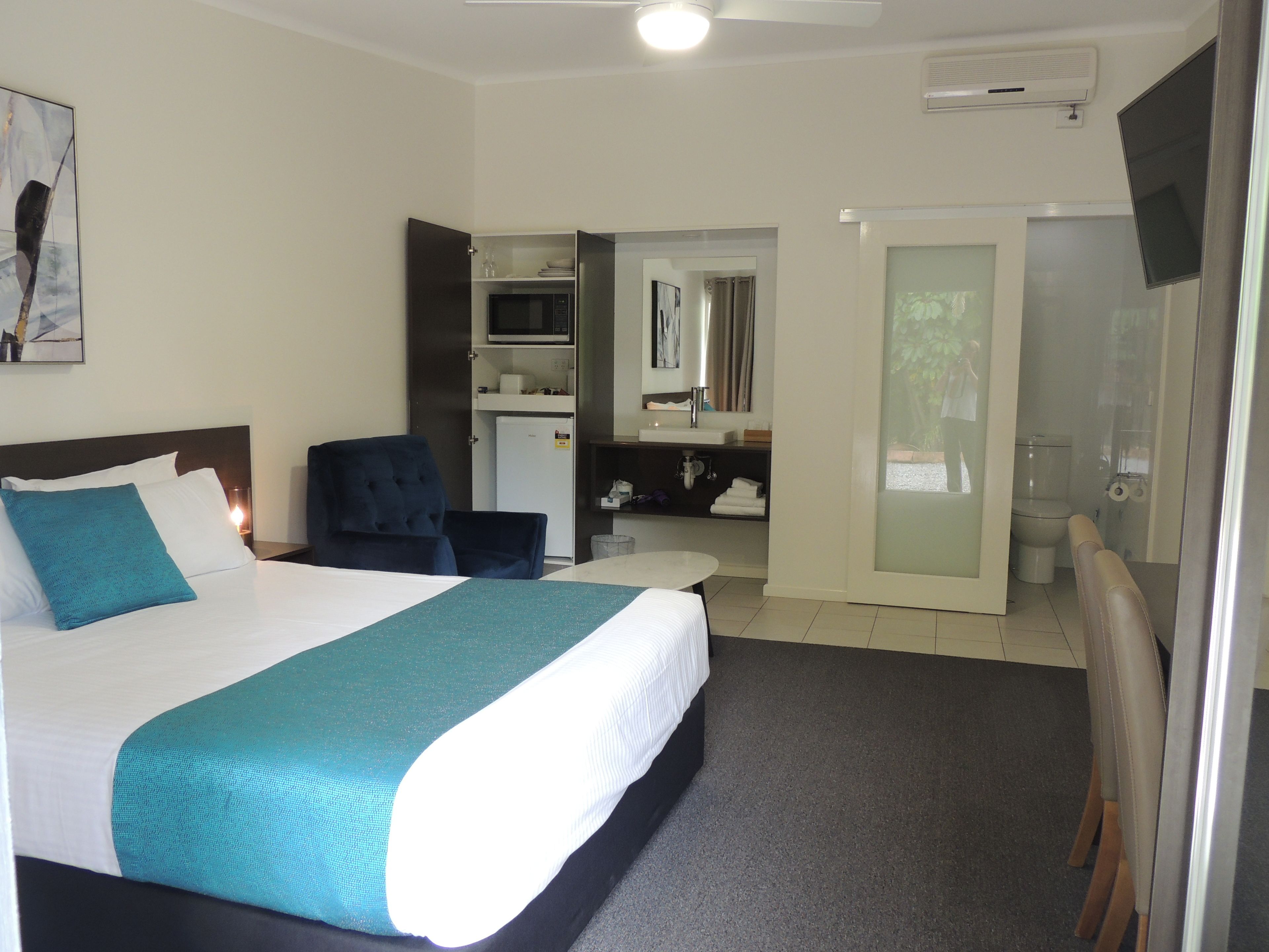 Habitación de hotel con cama, una silla, escritorio, microondas, lavabo e inodoro.