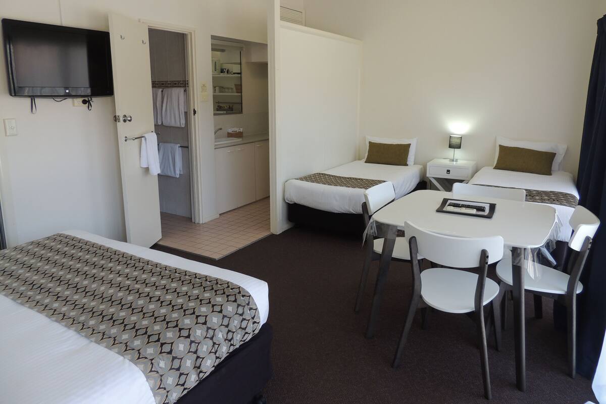 A hotel room with two beds, a TV, a desk with chairs, and a bathroom visible through an open door.