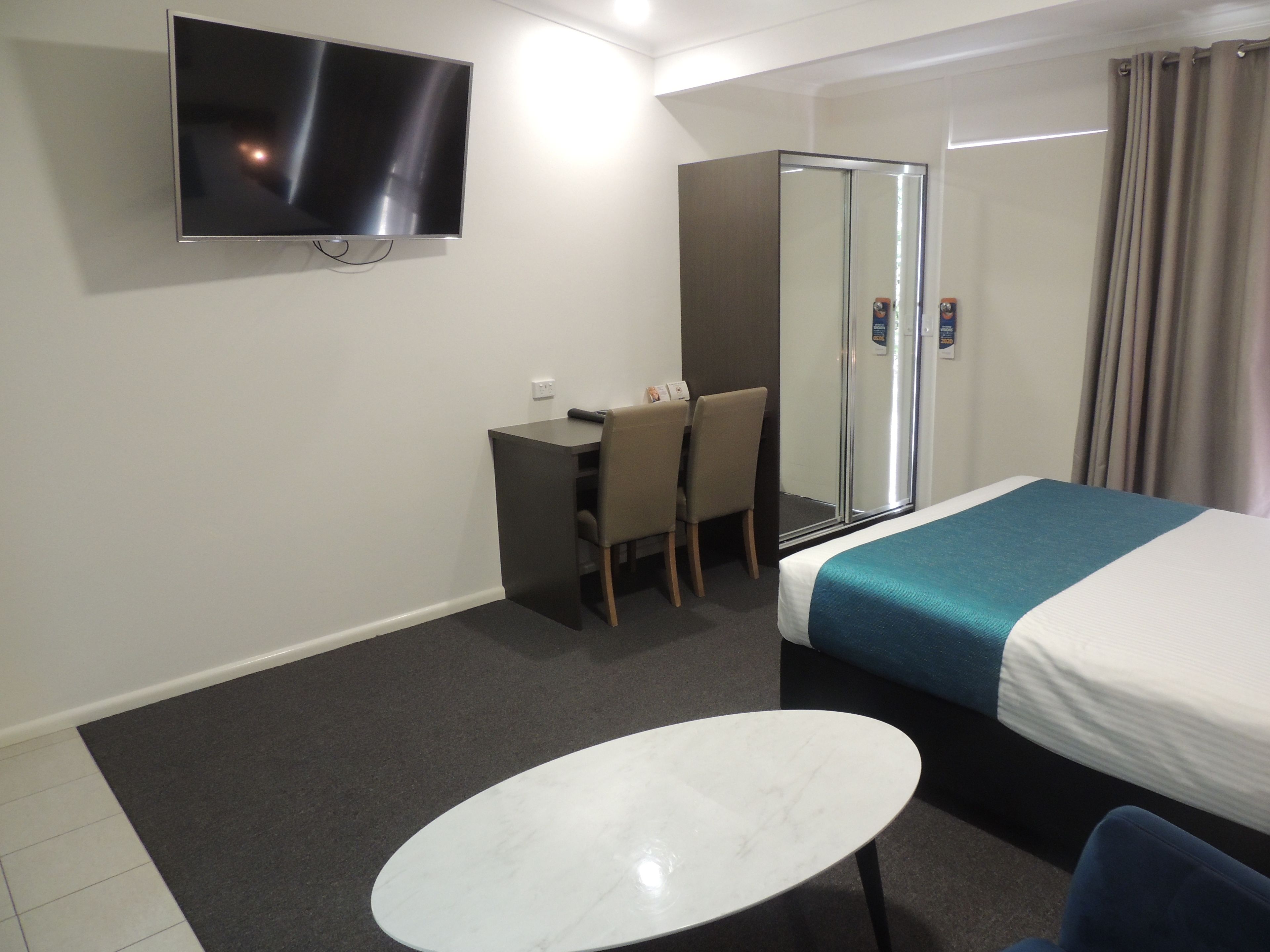 A hotel room with a bed, a desk, a chair, a TV, and a shower.