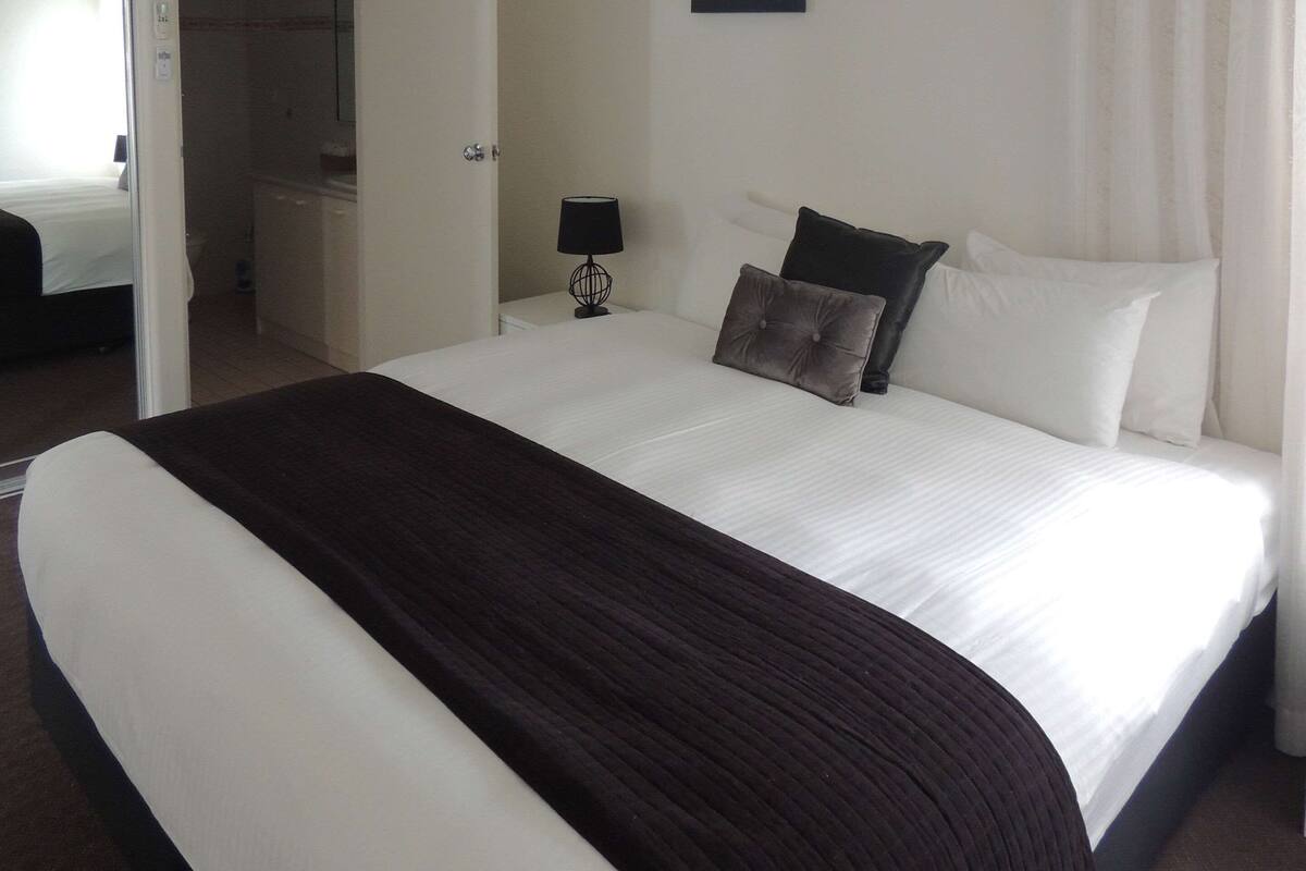 A neatly made bed with a dark brown bedspread, white pillows, and a small bedside table with a lamp.