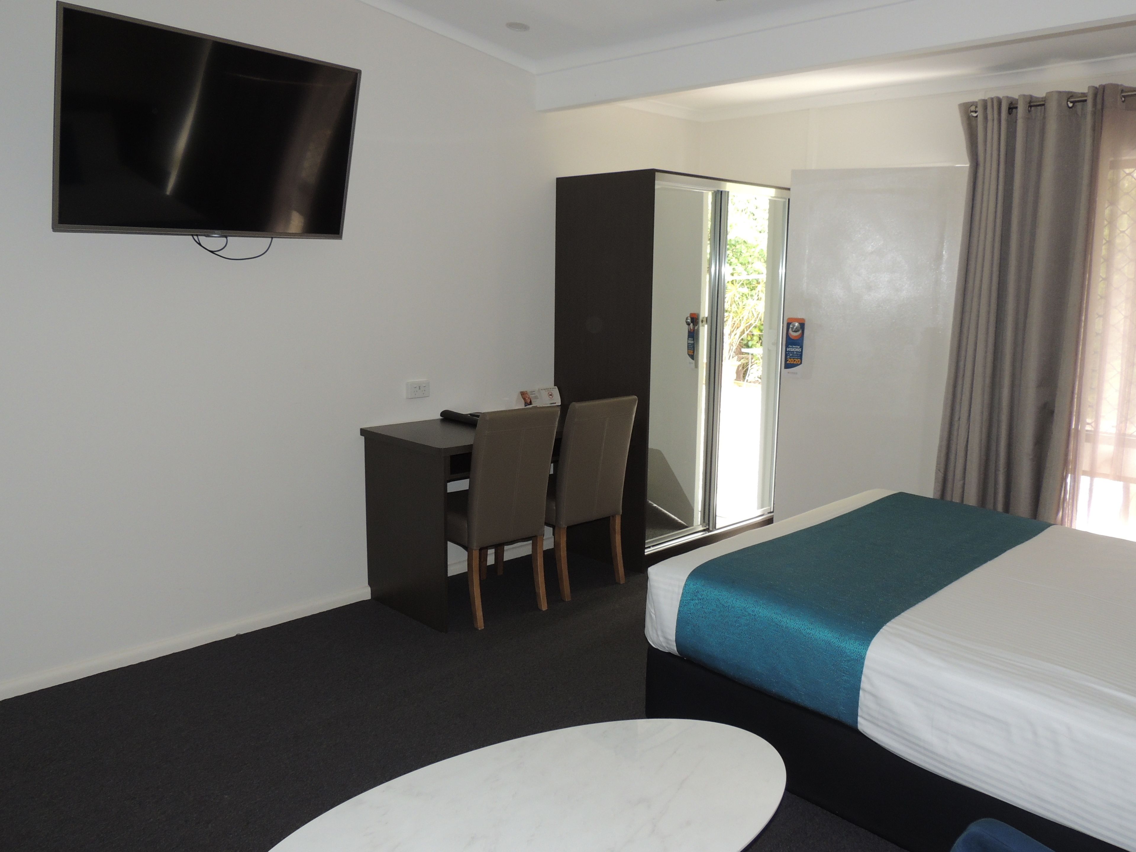 Een hotelkamer met een bed, een bureau, een stoel, een televisie en een kledingkast.
