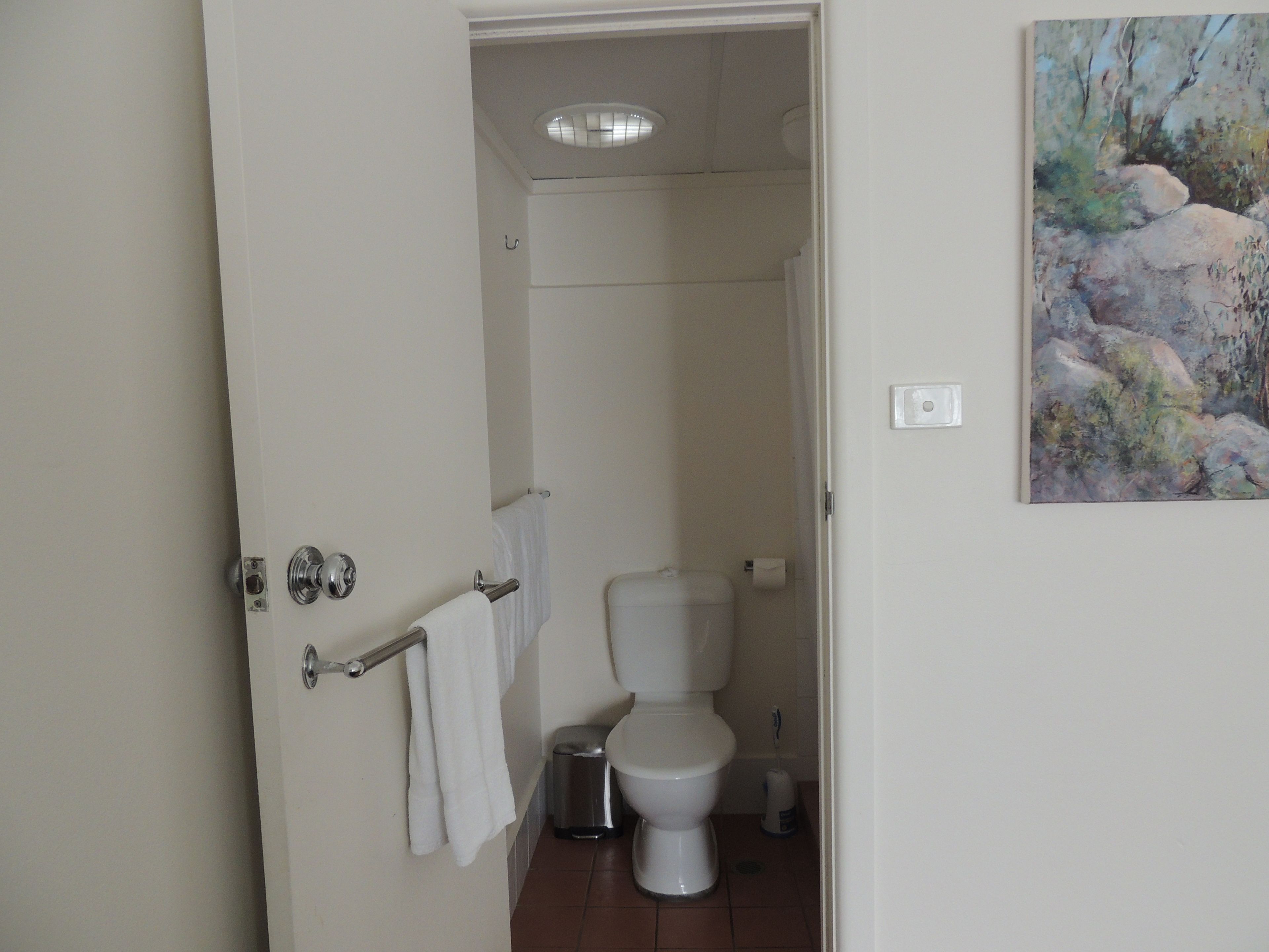 A bathroom with a toilet, a trash bin, and a towel rack.