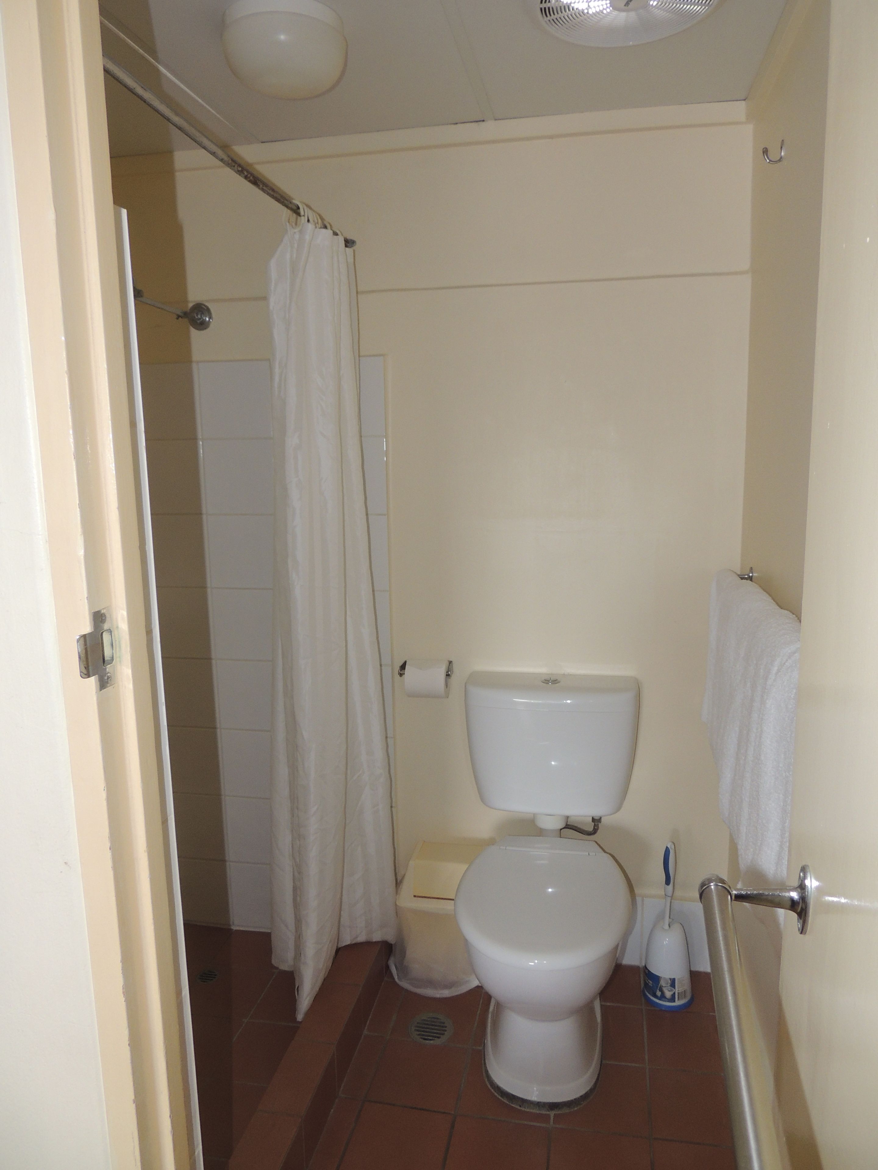 A small, basic bathroom with a toilet, a shower curtain, a toilet paper holder, and a hand dryer.