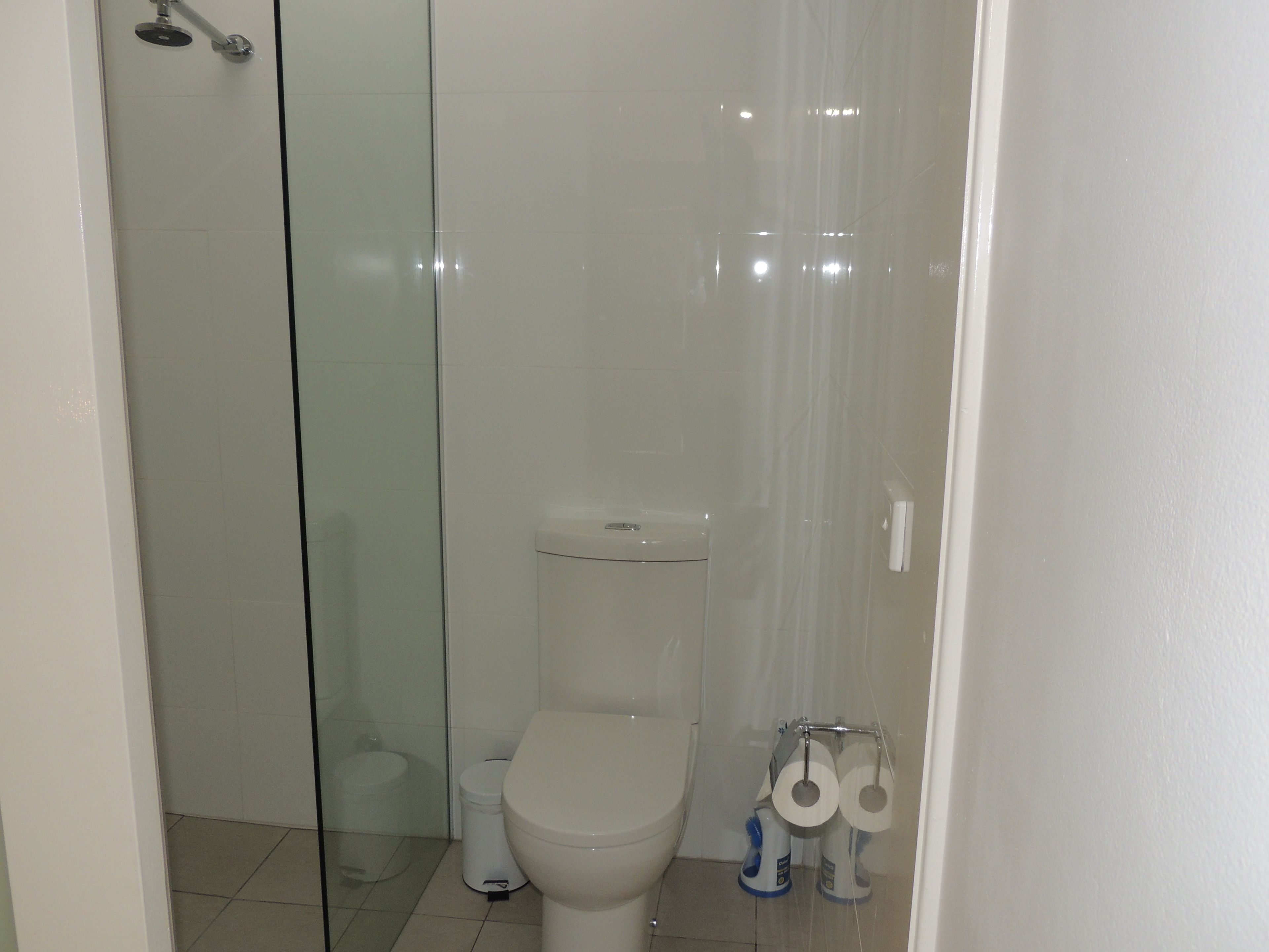 A bathroom with a glass shower enclosure, a toilet, and a toilet paper holder.
