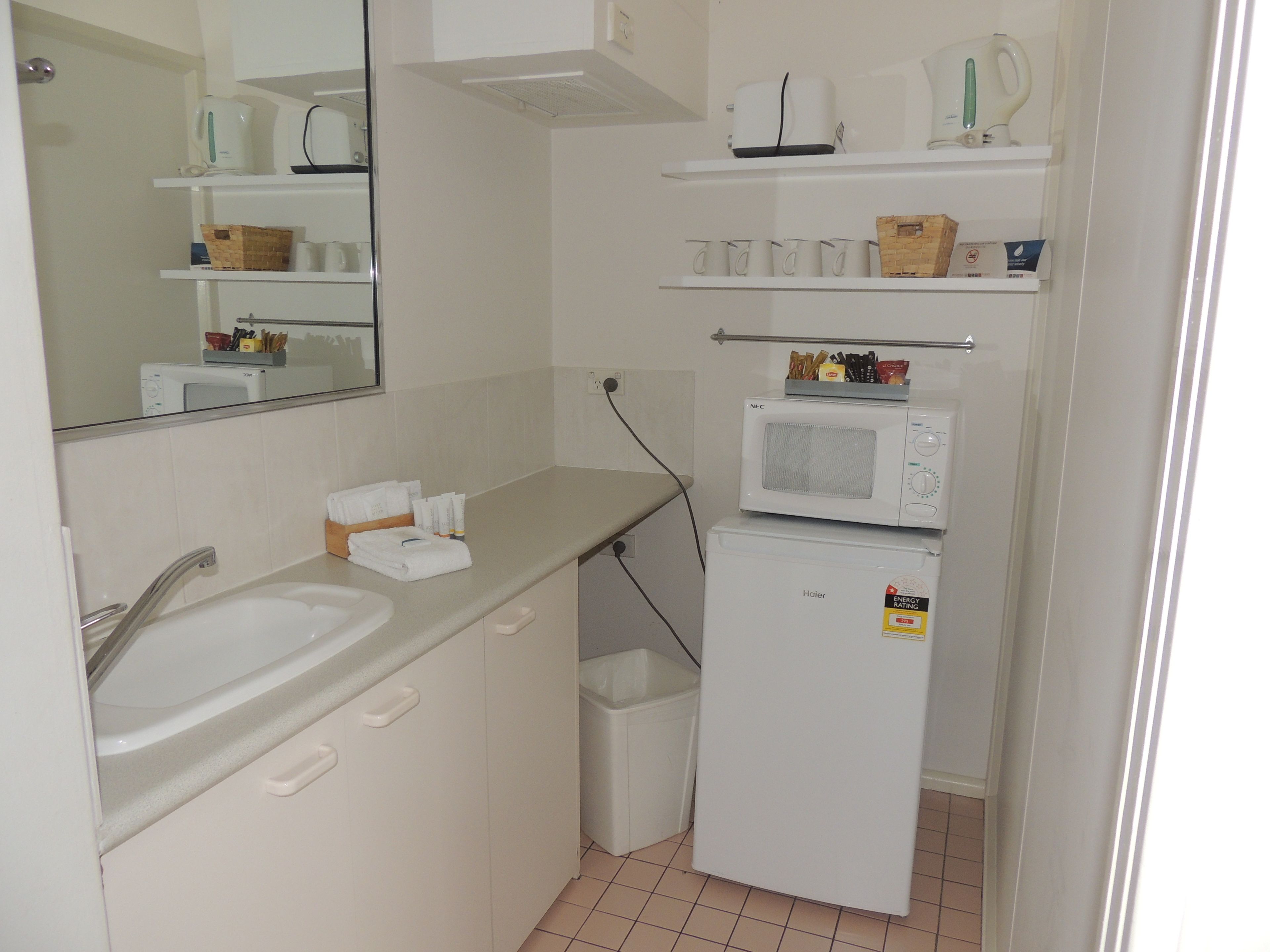 Una pequeña kitchenette con pileta, microondas y estanterías.