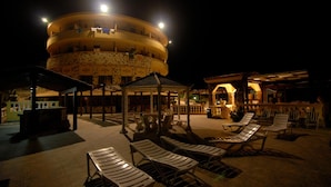 A circular building with multiple balconies, a covered seating area with lounge chairs, and a well-lit outdoor space. - Hotel Restaurant Diana (Ustica)