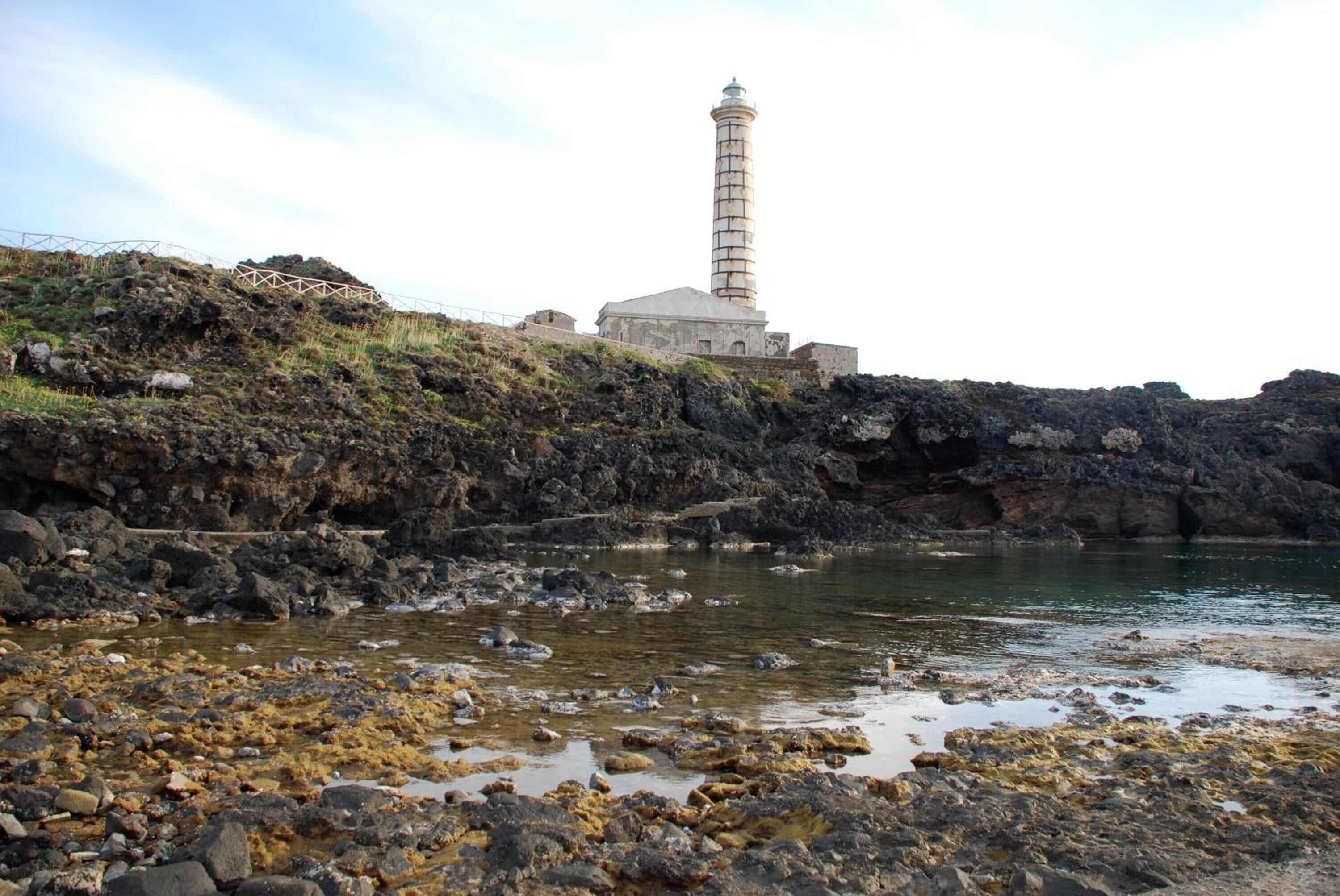 A coastal scene with a lighthouse, rocky shoreline, and calm water.