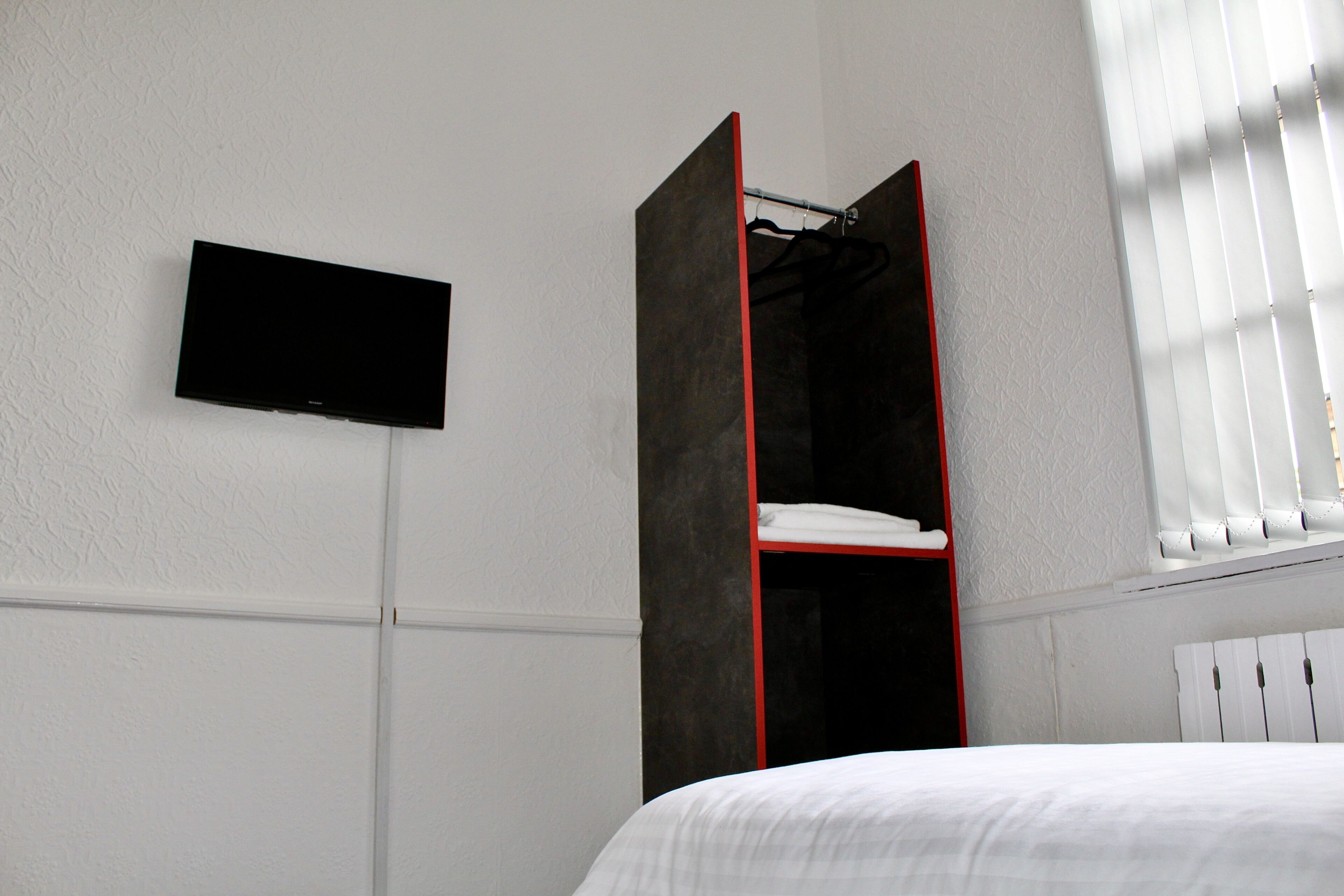 A bedroom with a bed, a TV mounted on the wall, and a wardrobe with a red frame.