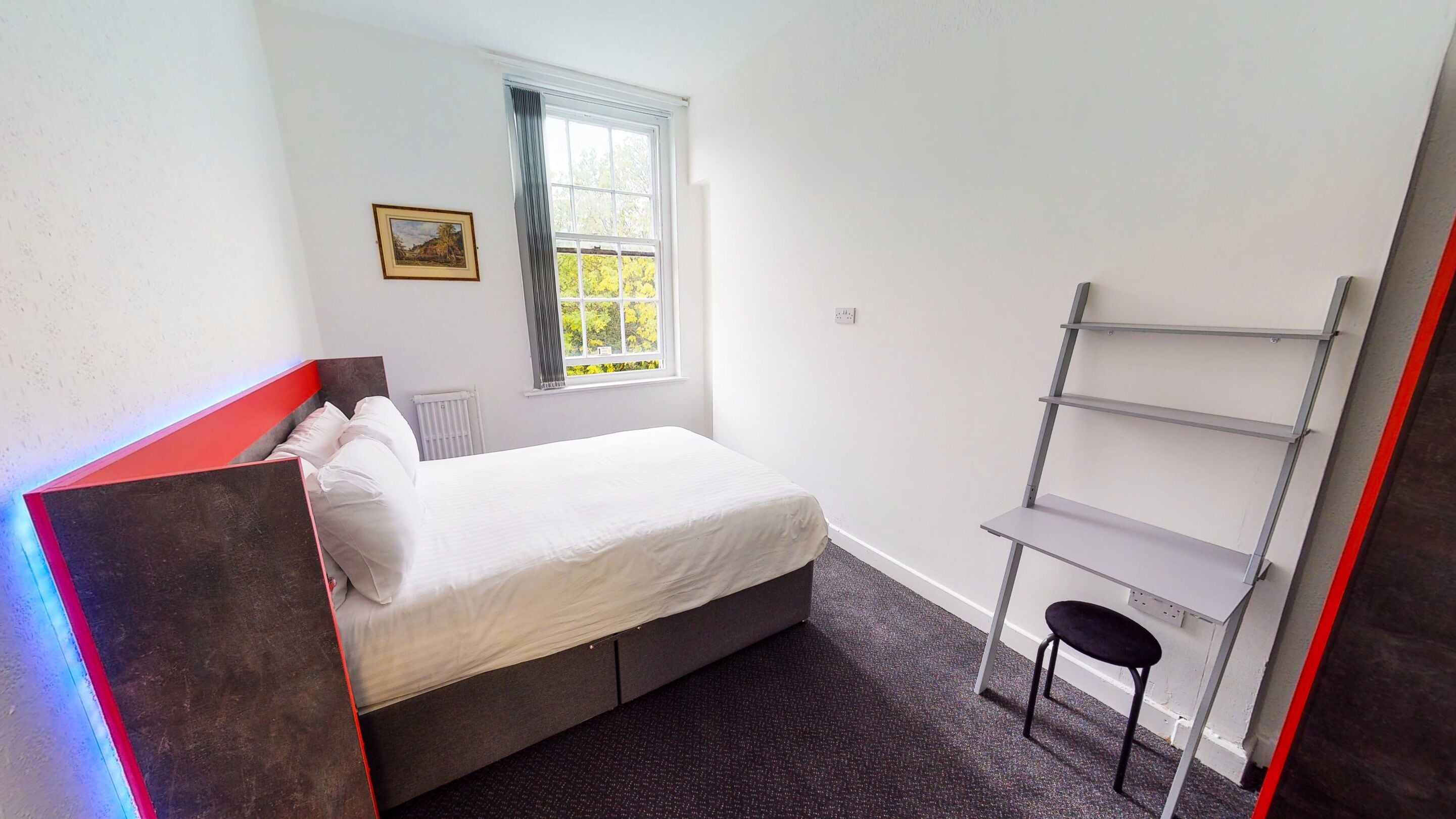 A bedroom with a bed, a radiator, a window with curtains, a picture on the wall, and a shelf unit.