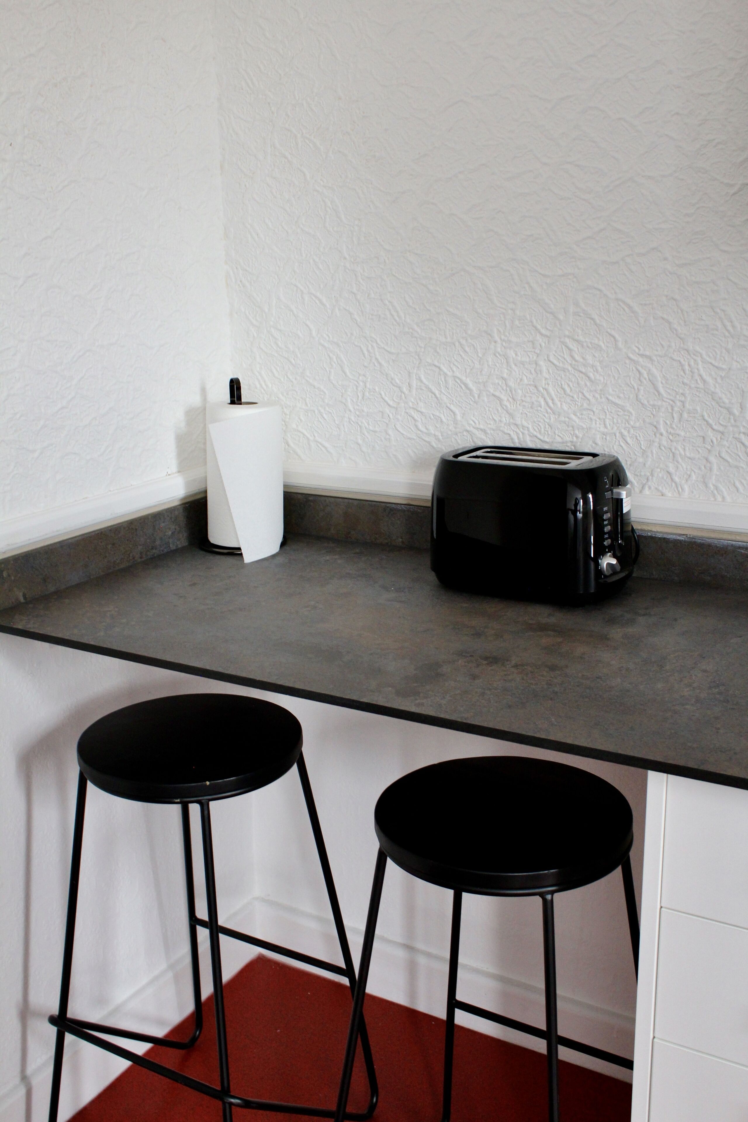 Una encimera de cocina con un tostador, un dispensador de toallas de papel blancas y dos taburetes negros.