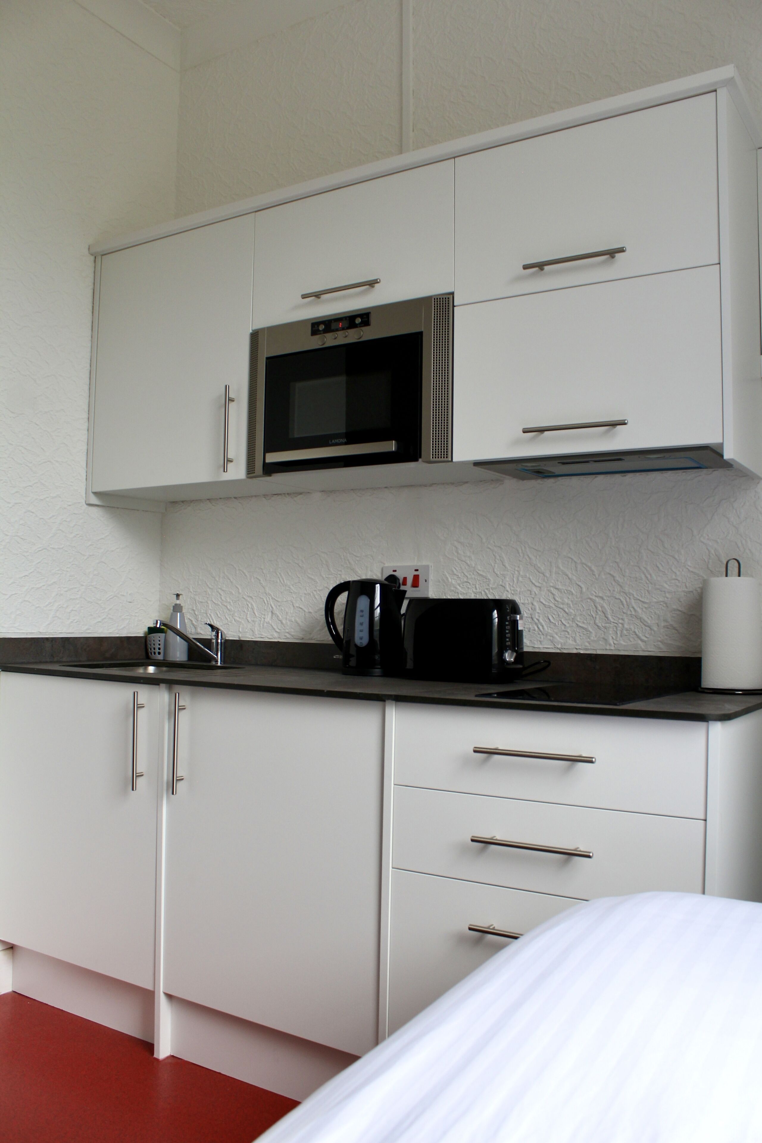 A compact kitchenette with a microwave, toaster, kettle, and a small sink.