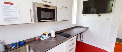 A modern kitchen with white cabinets, a stainless steel sink, a microwave, and a flat-screen TV mounted on the wall.