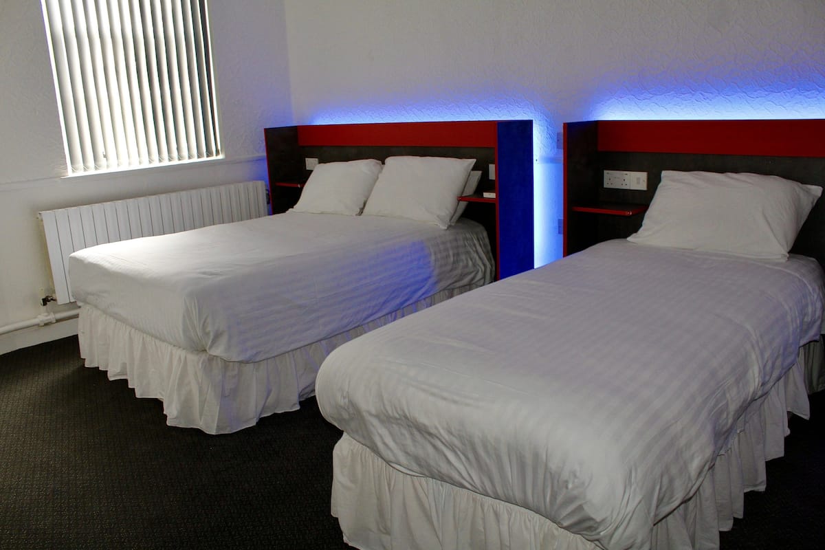 A hotel room with two single beds, a red accent wall, and a window with blinds.