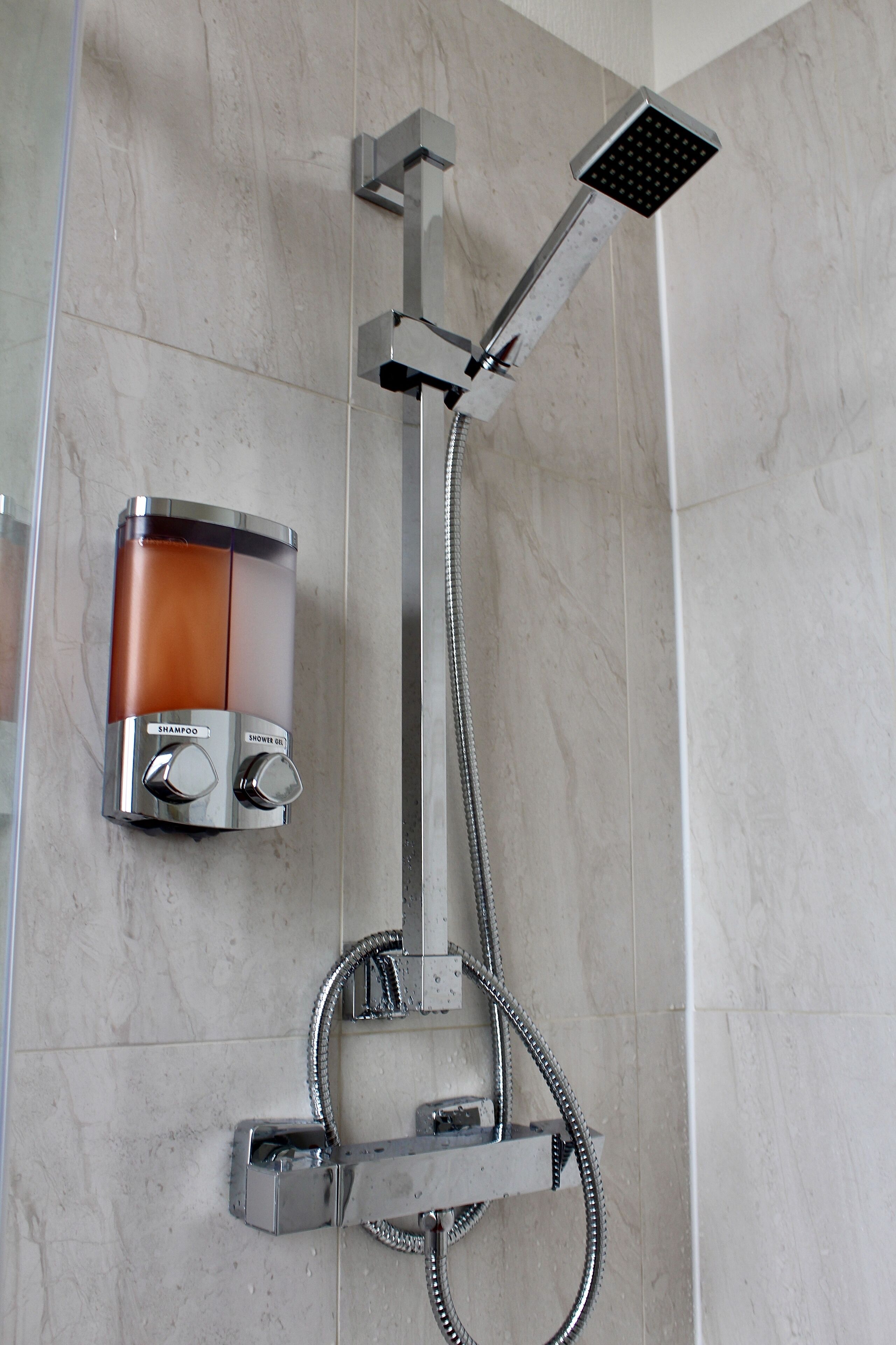 A modern shower with a handheld showerhead and a fixed showerhead, both mounted on a wall.