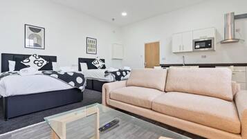 A modern hotel room with two beds, a sofa, a glass coffee table, and a kitchenette.
