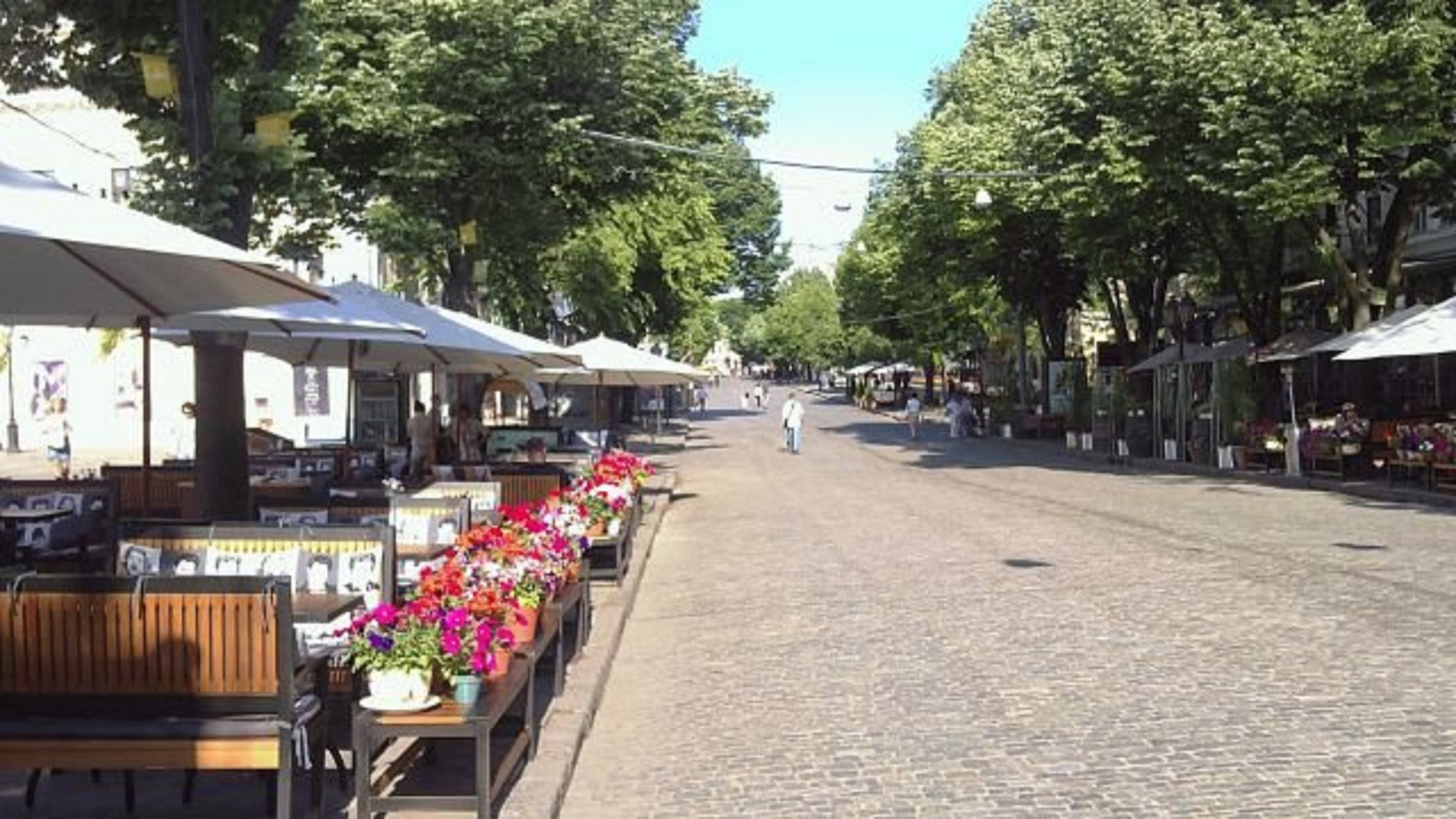 A cobblestone street lined with outdoor cafes and flower stalls.