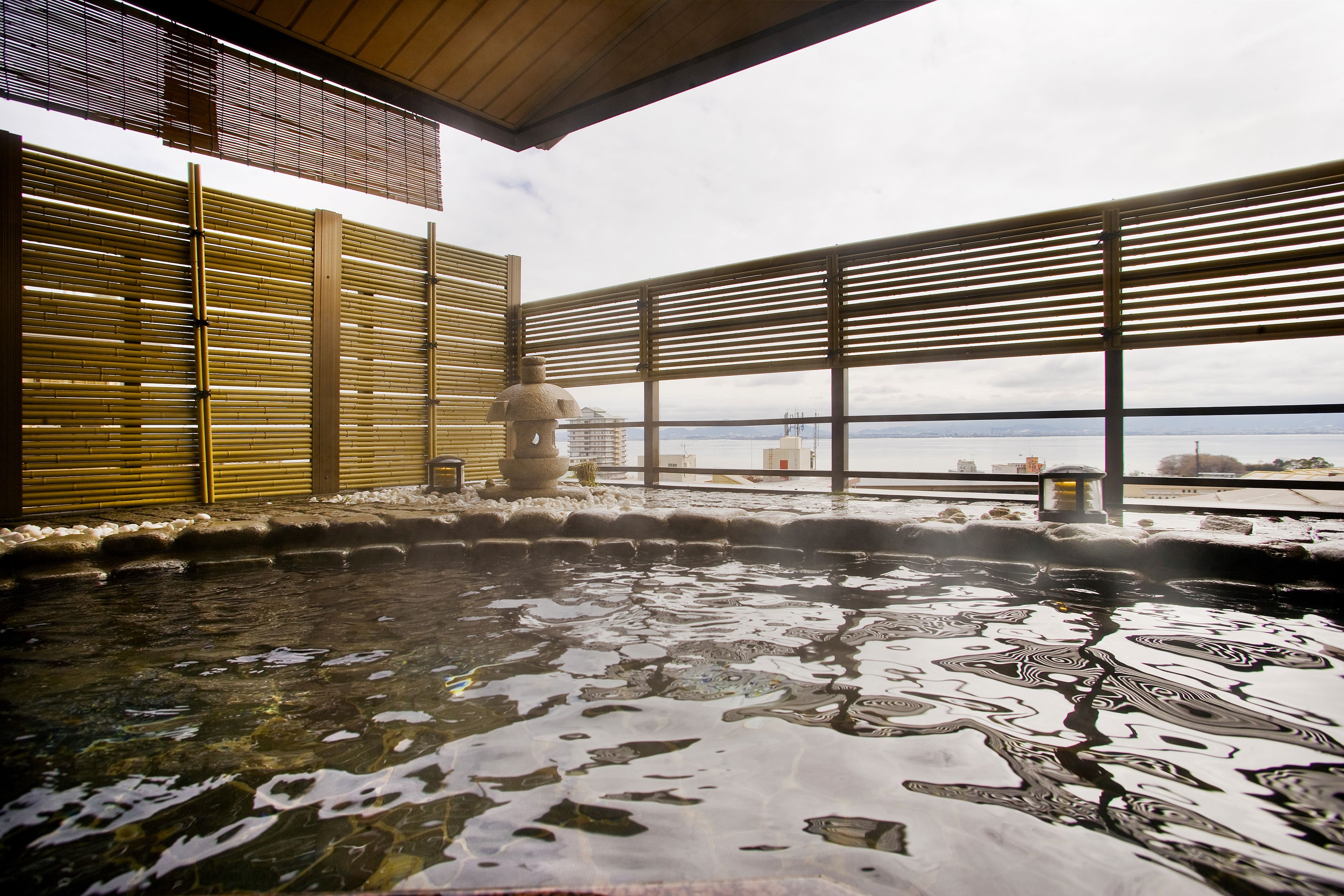 A hot spring bath area with wooden sliding doors, a stone sculpture, and a view of distant buildings.