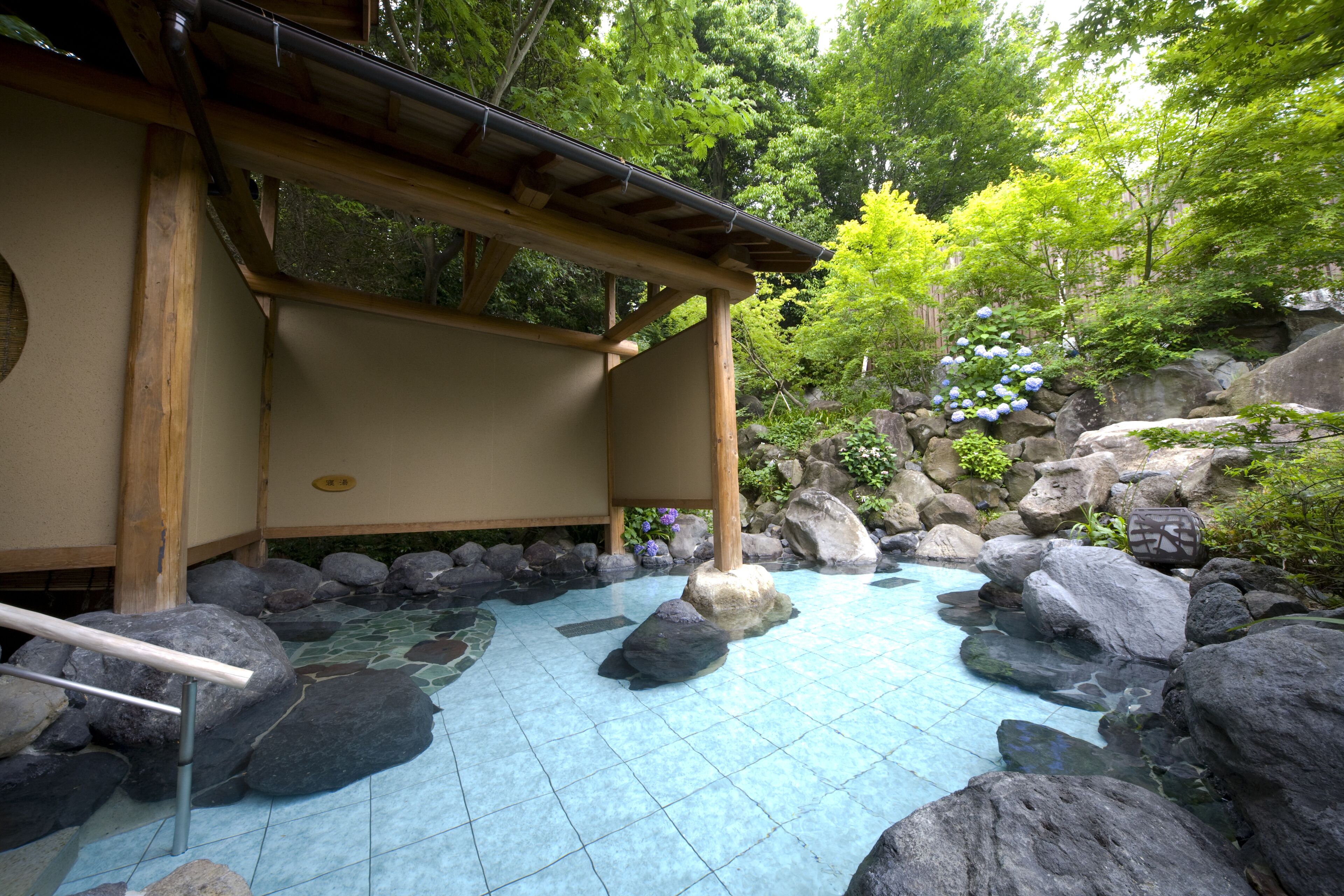 A traditional Japanese garden with a wooden structure, a koi pond, and large rocks.