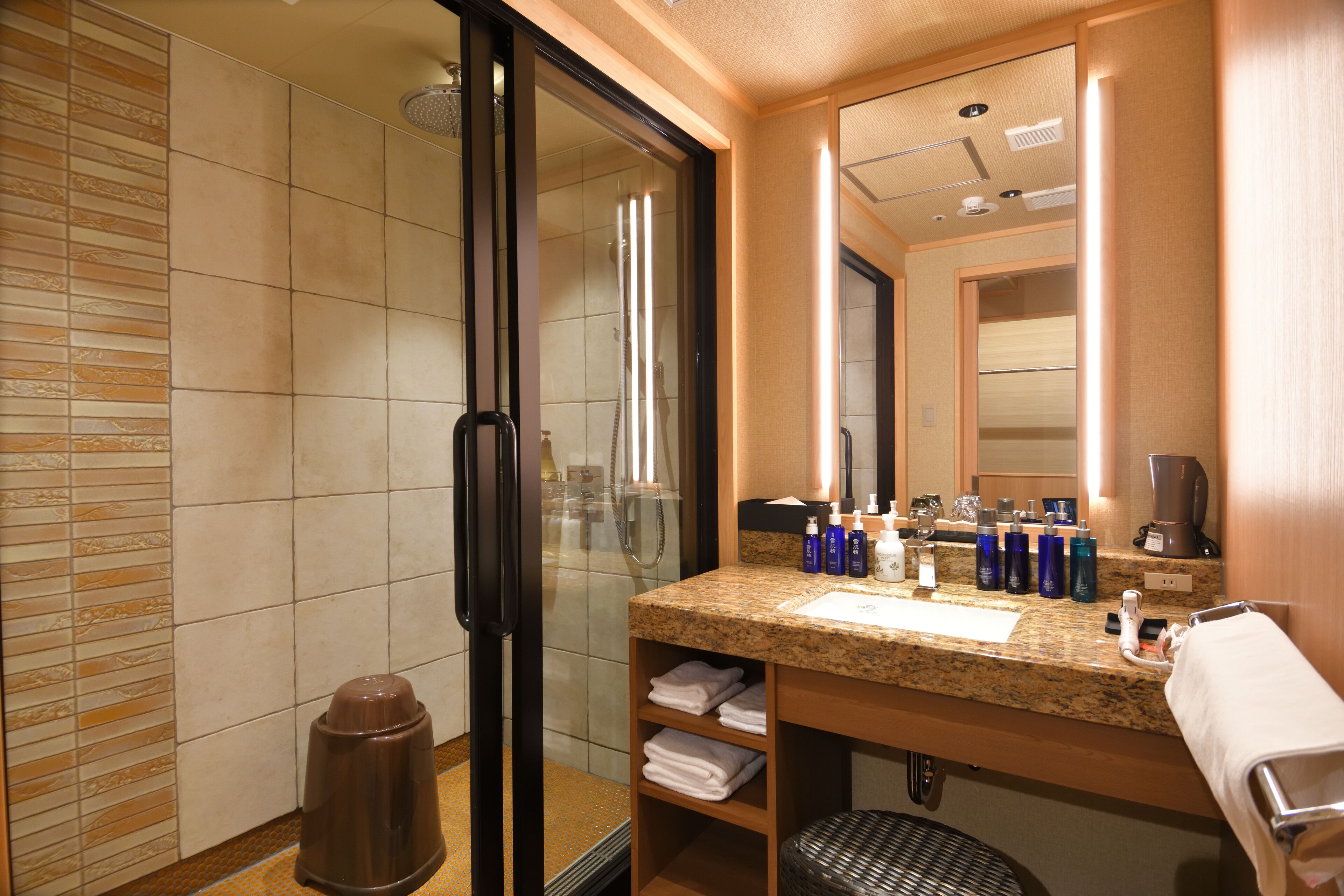 A modern bathroom with a glass shower enclosure, a granite countertop, and a large mirror.