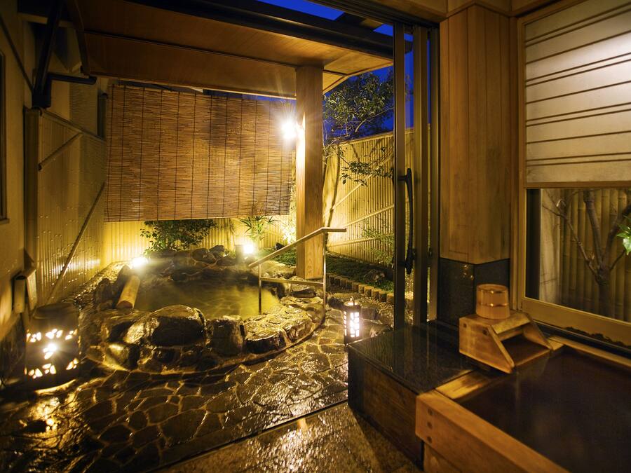 Ein traditionelles japanisches Onsen mit einem Steingrund-Bad, hölzernen Bänken und einem Bambuszaun.