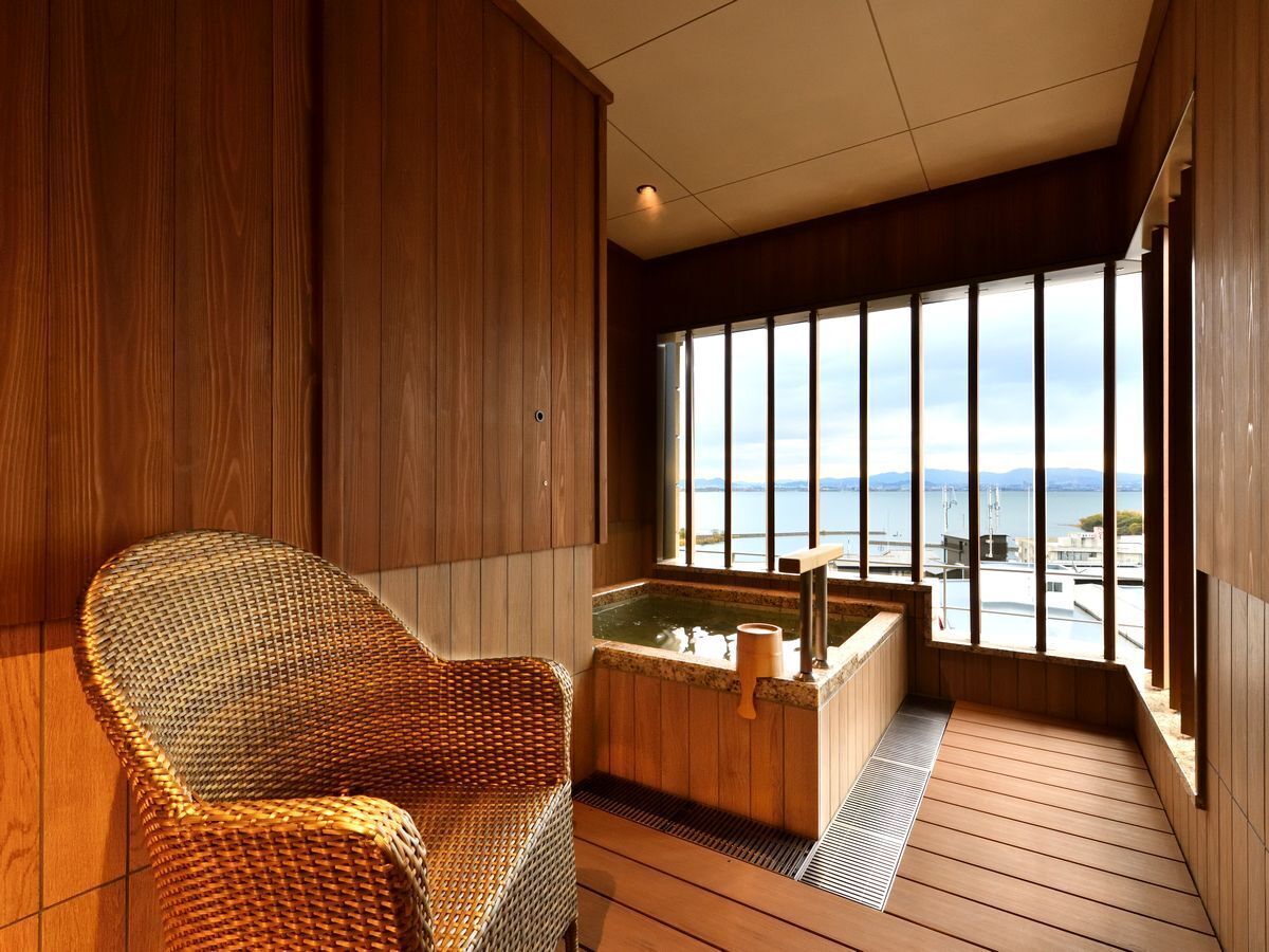 A wooden-floored room with a large window, a wicker chair, and a hot tub.