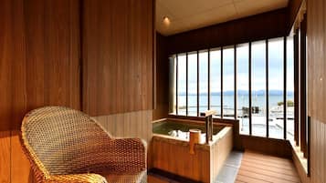 A wooden-floored room with a large window, a wicker chair, and a hot tub.