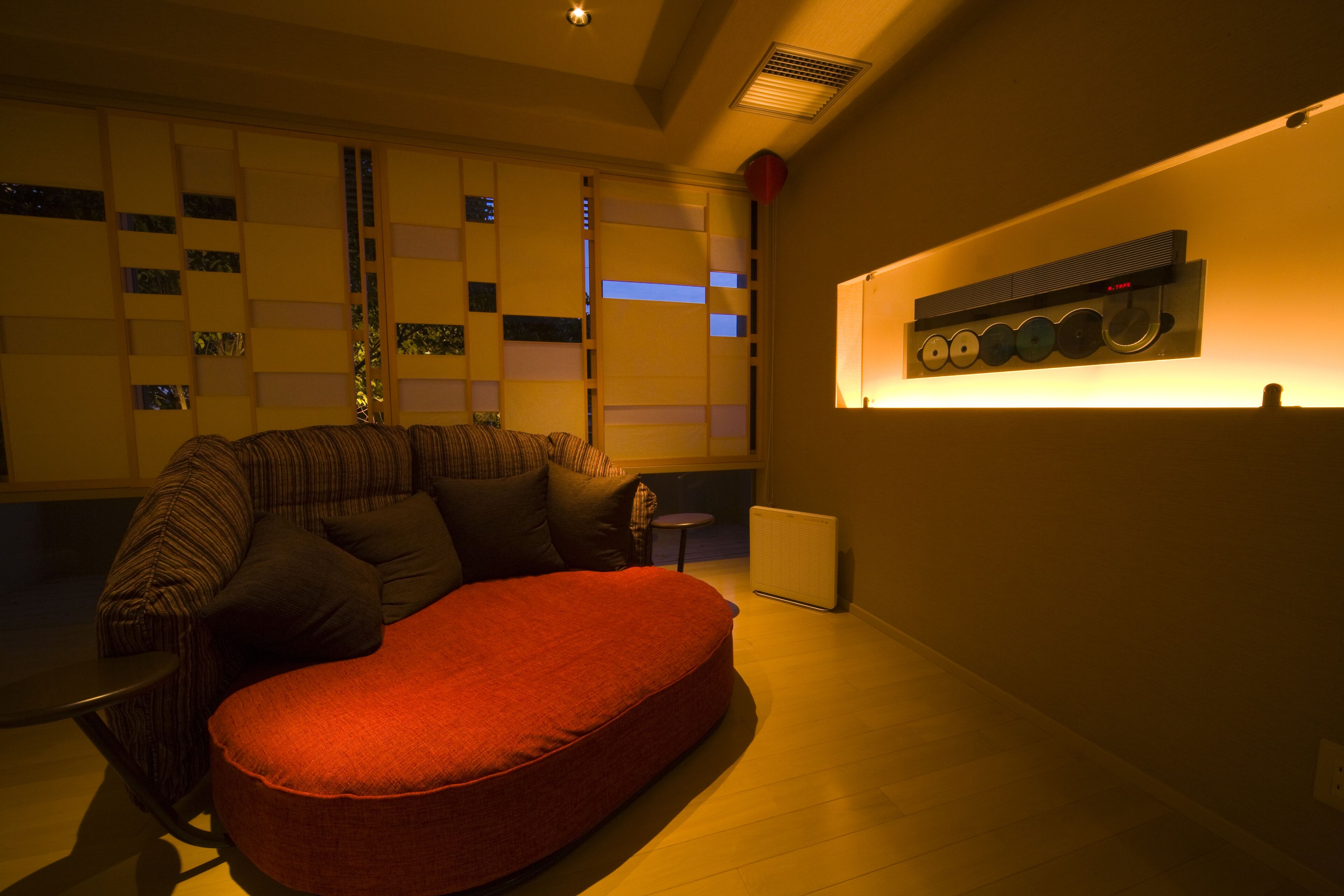 Uma sala de estar moderna com um sofá, um banquinho vermelho, um radiador e um aparelho de ar condicionado fixado na parede.