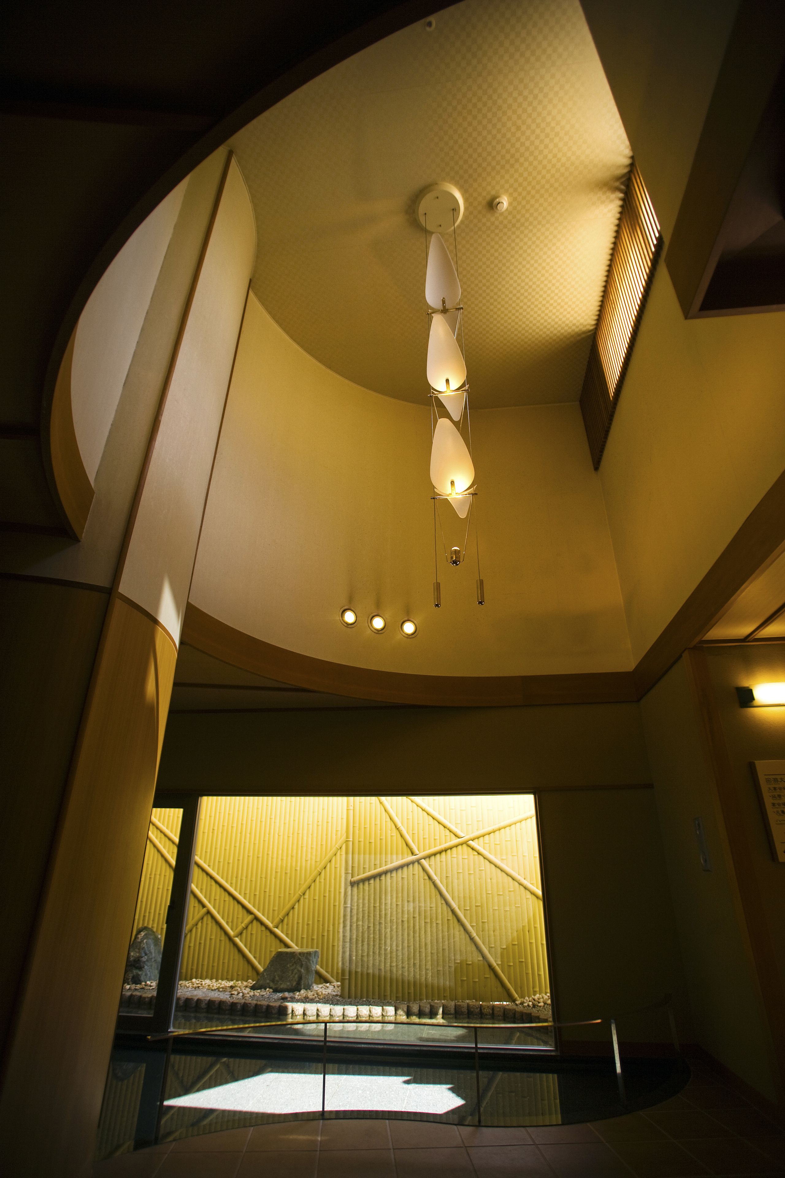 Un interior moderno con un diseño de techo único, una barandilla de cristal y vistas a una estructura de bambú exterior.