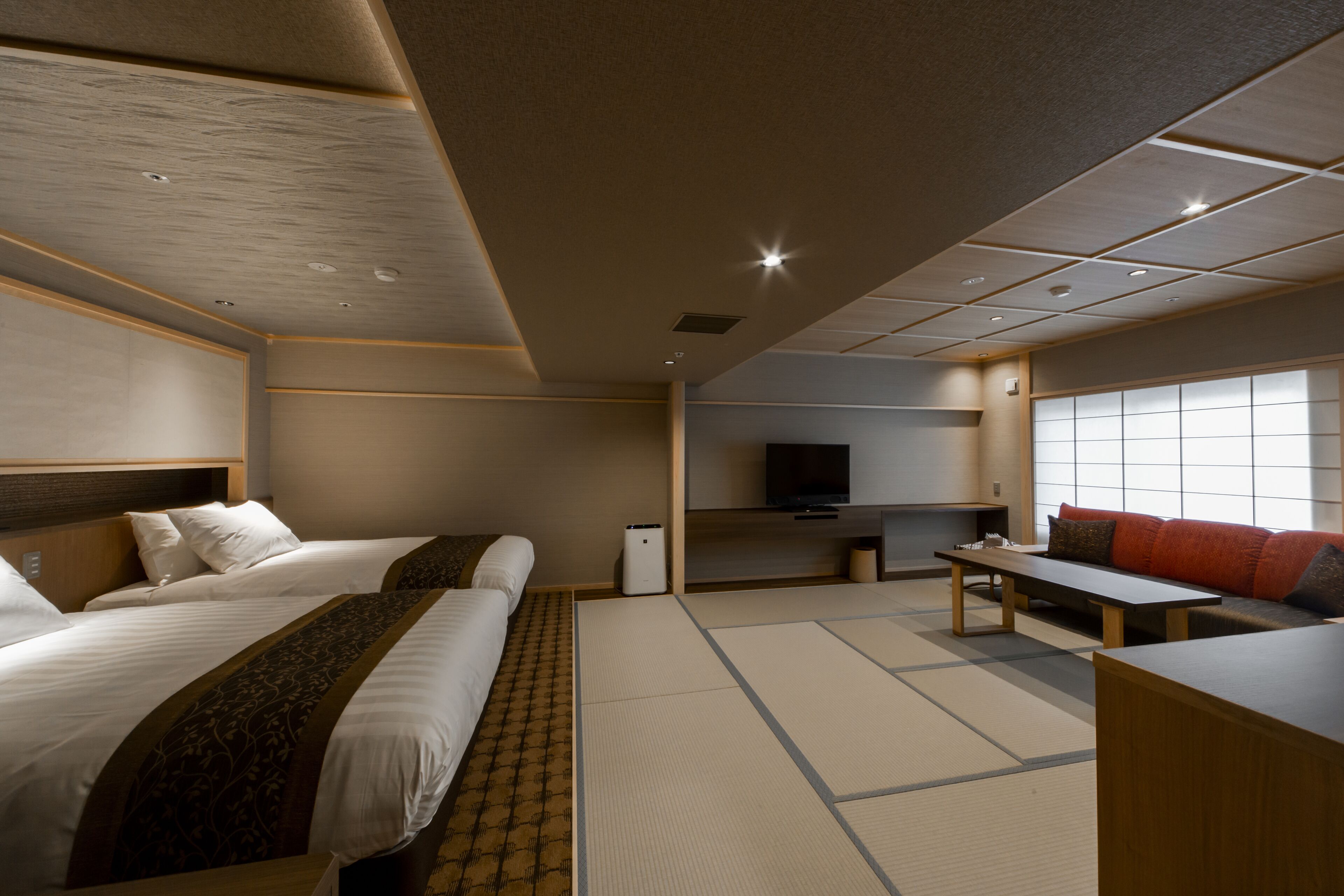 Habitación de hotel con dos camas, televisión, sofá, mesa y suelo de tatami.