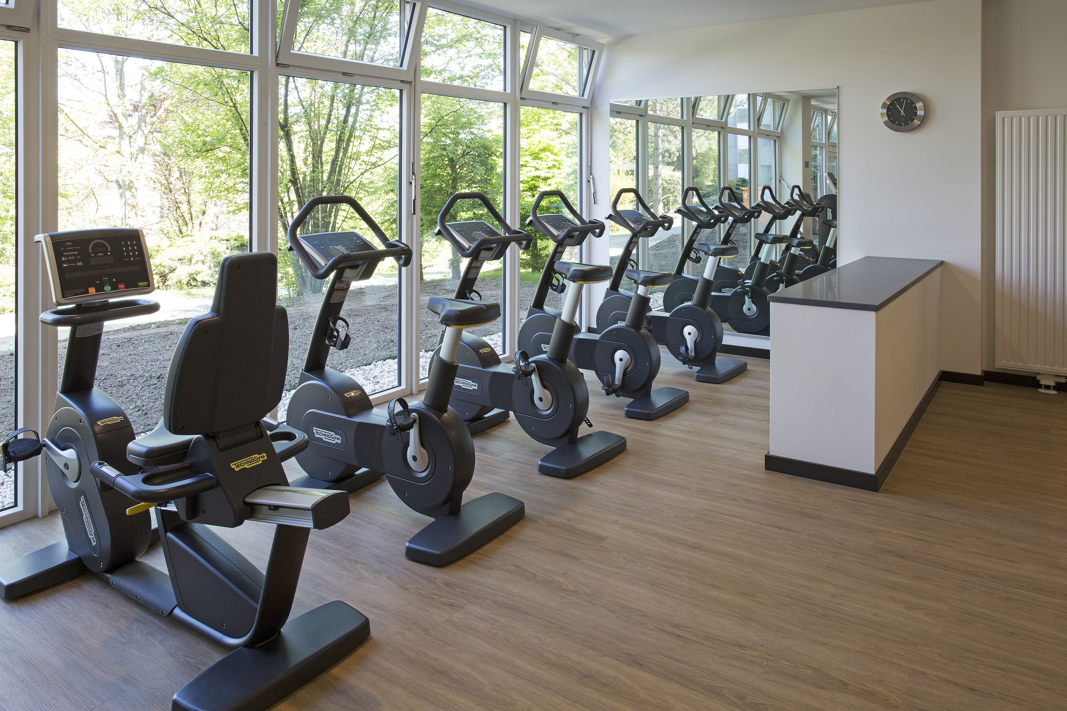 A gym with multiple stationary bikes and a control panel, large windows, and a white reception desk.