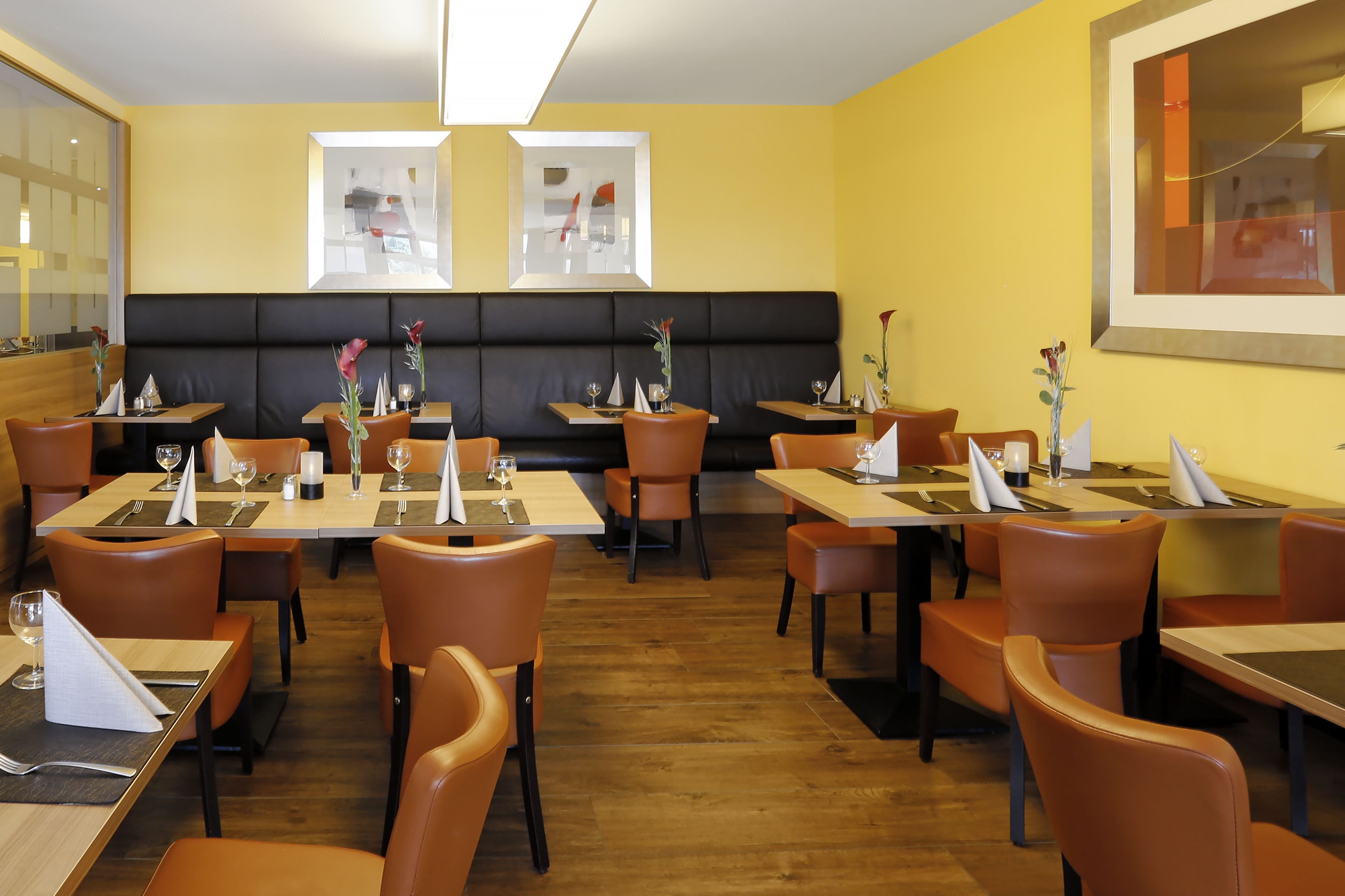 A restaurant with booths and tables, wooden flooring, and yellow walls.