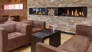 Un espace de détente moderne avec des canapés en cuir, une table basse noire et un mur en pierre agrémenté d’une cheminée.