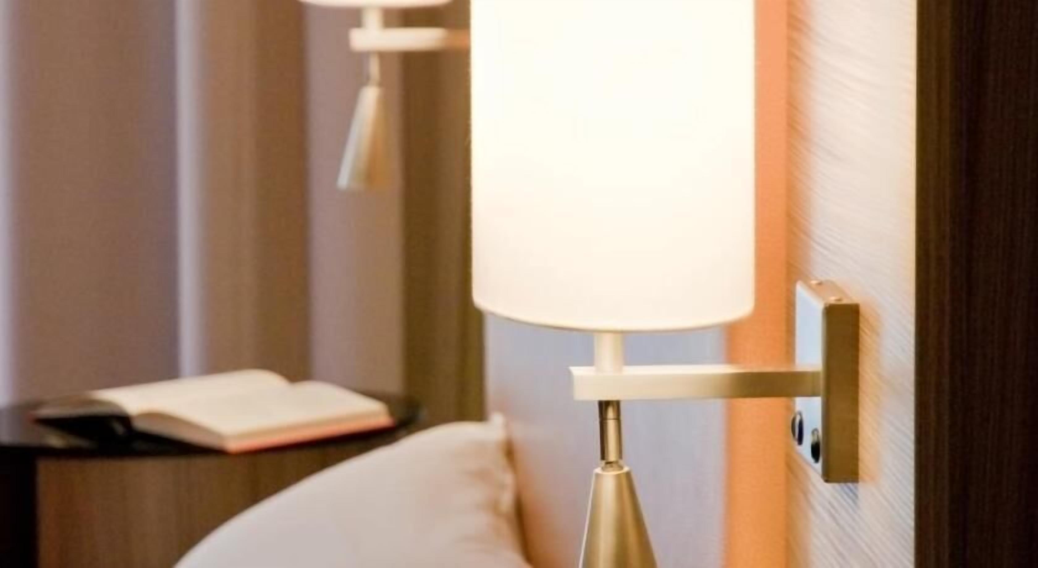 A hotel room with a bedside lamp, a nightstand, and an open book.