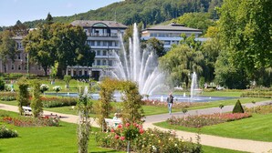 Un parc avec une fontaine, des allées et des parterres de fleurs.