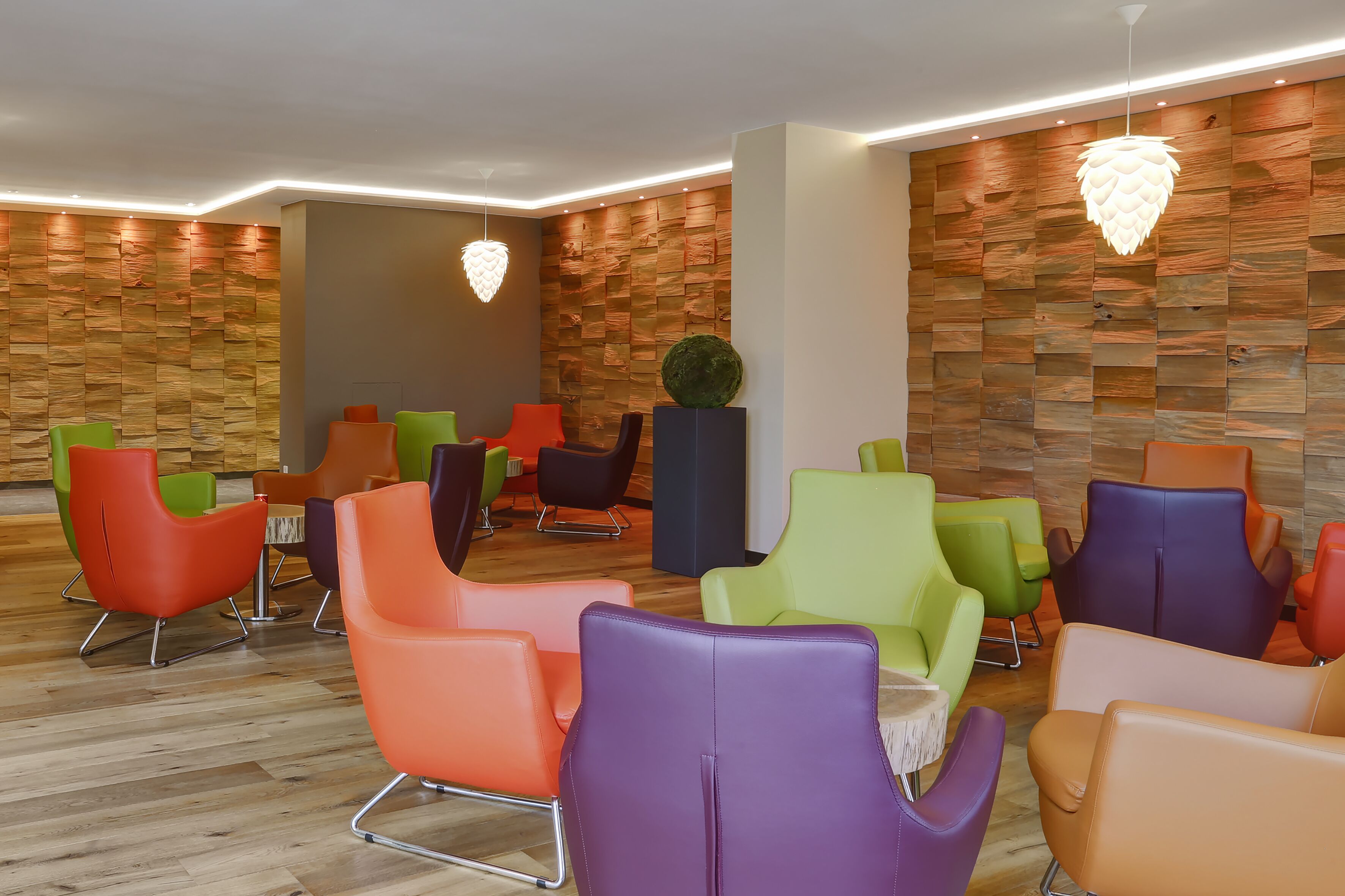 A modern lounge area with colorful chairs and a wooden wall.