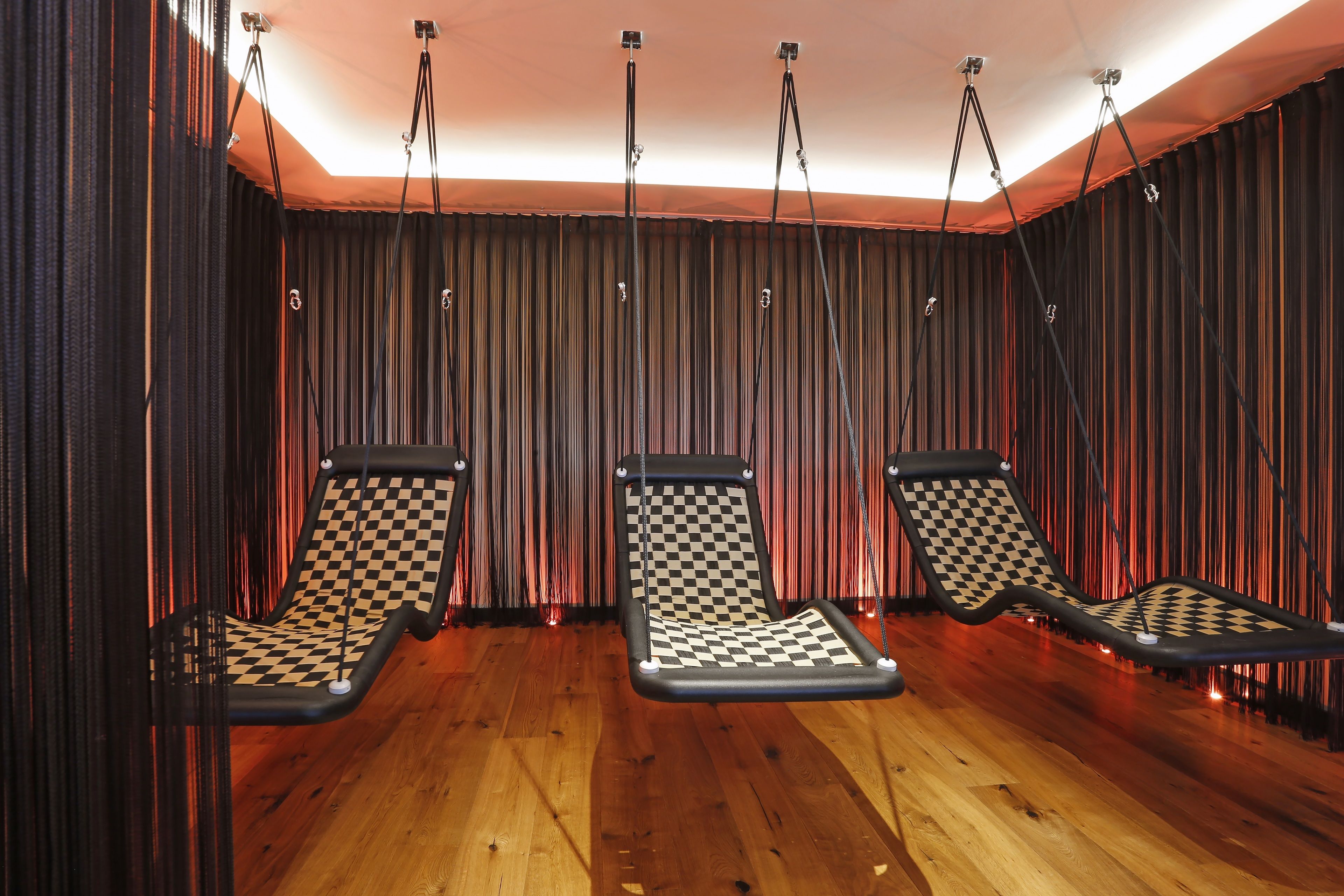 Una habitación con tres sillones de sala colgantes a techo, con estampado de cuadros blancos y negros, piso de madera y un telón de fondo.