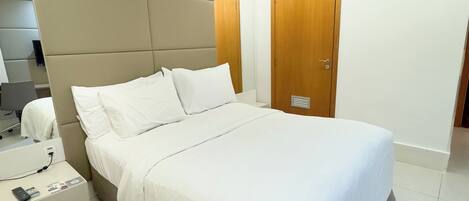 Une chambre d’hôtel moderne dotée d’un grand lit, d’une table de chevet avec un téléphone et une télécommande, d’un climatiseur fixé au mur et d’une porte en bois.